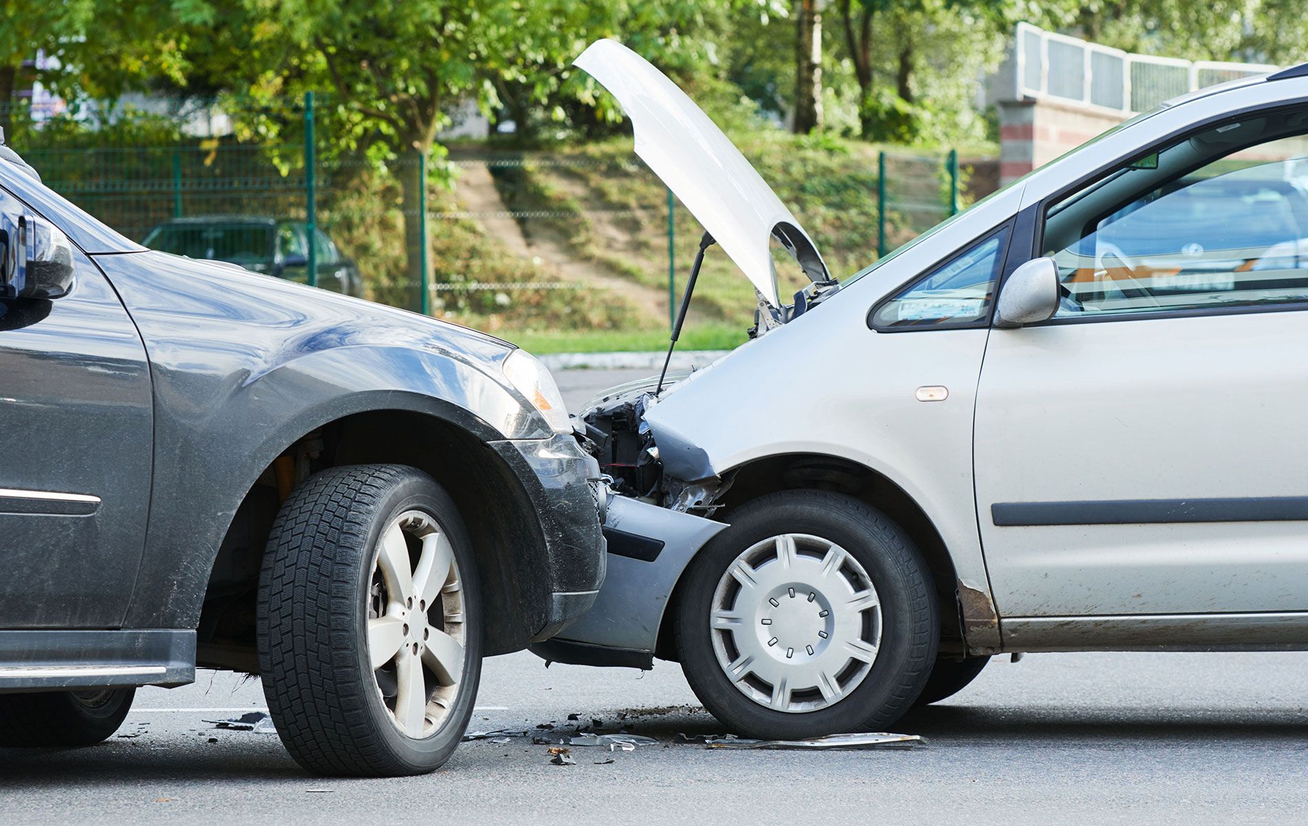 Two cars crashed head-on; gray car's front against a silver car's front, hood open, on a paved road.