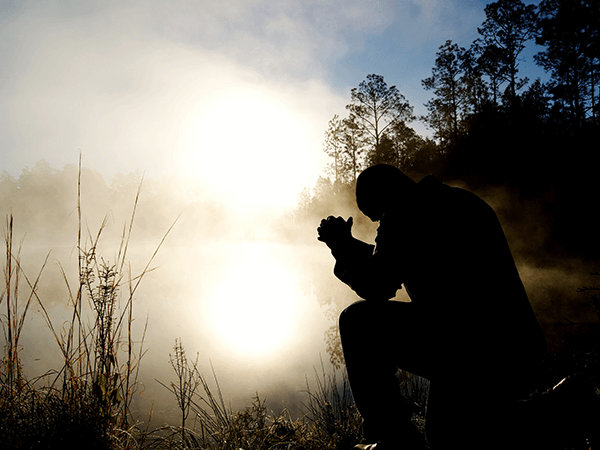 Silhouette of a person crouching in a smoky field at sunrise, holding a cup near the face
