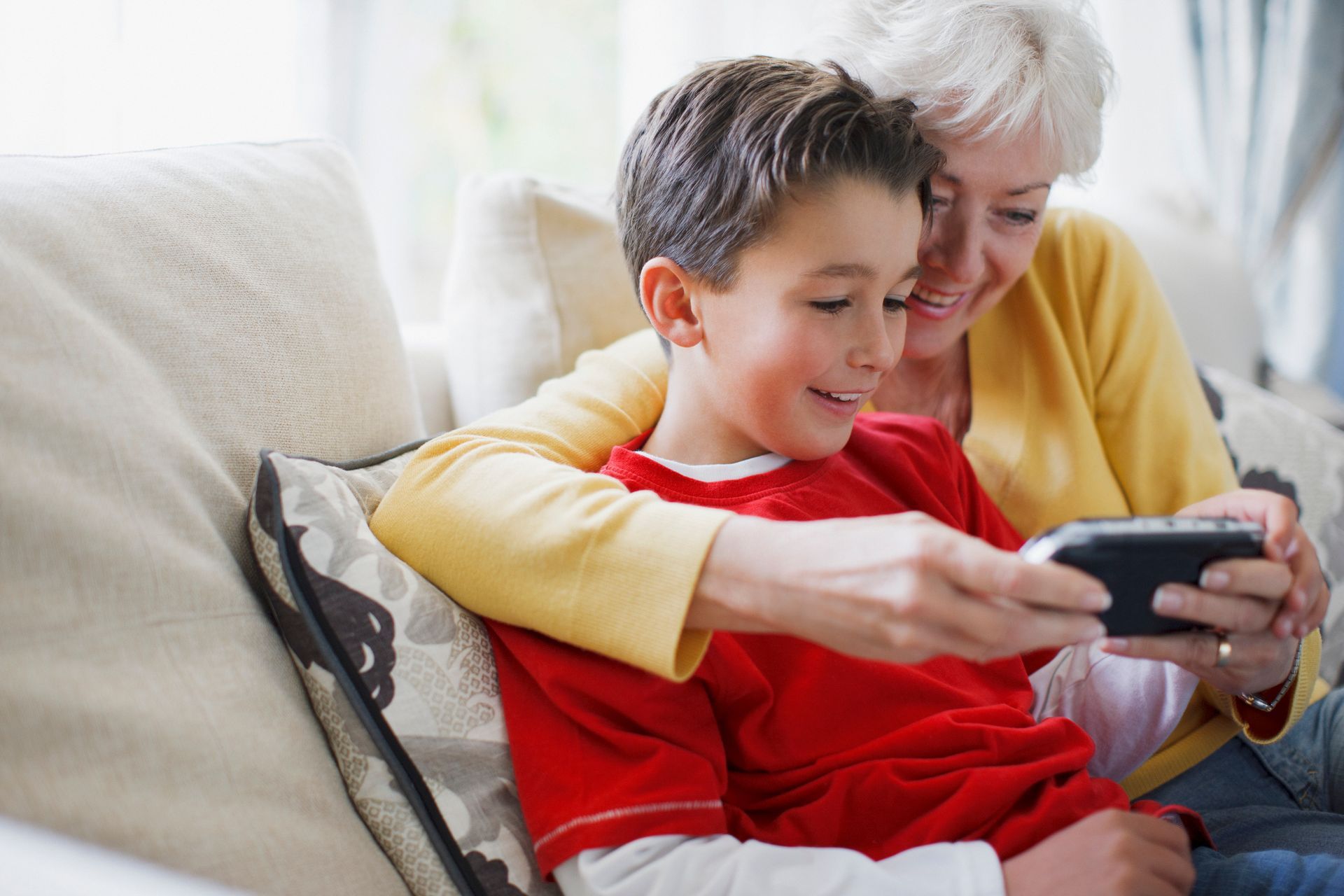Older woman and child smiling on a couch while looking at a smartphone together