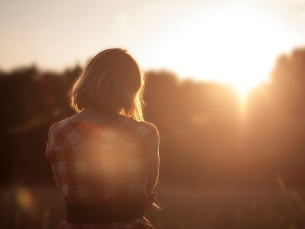 Backlit person standing outdoors at sunset, facing a glowing horizon.