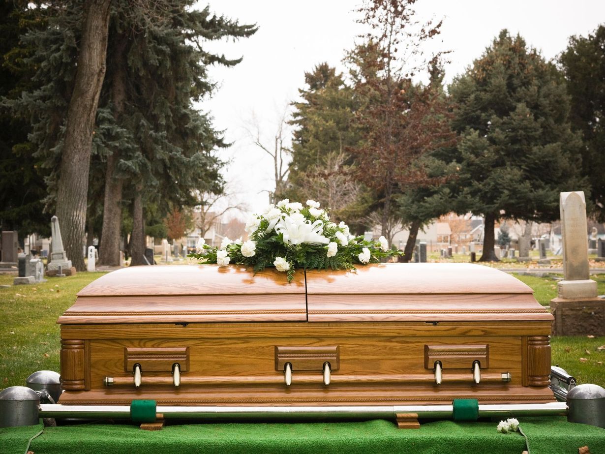 Wooden coffin with white flowers in a cemetery, surrounded by gravestones and trees