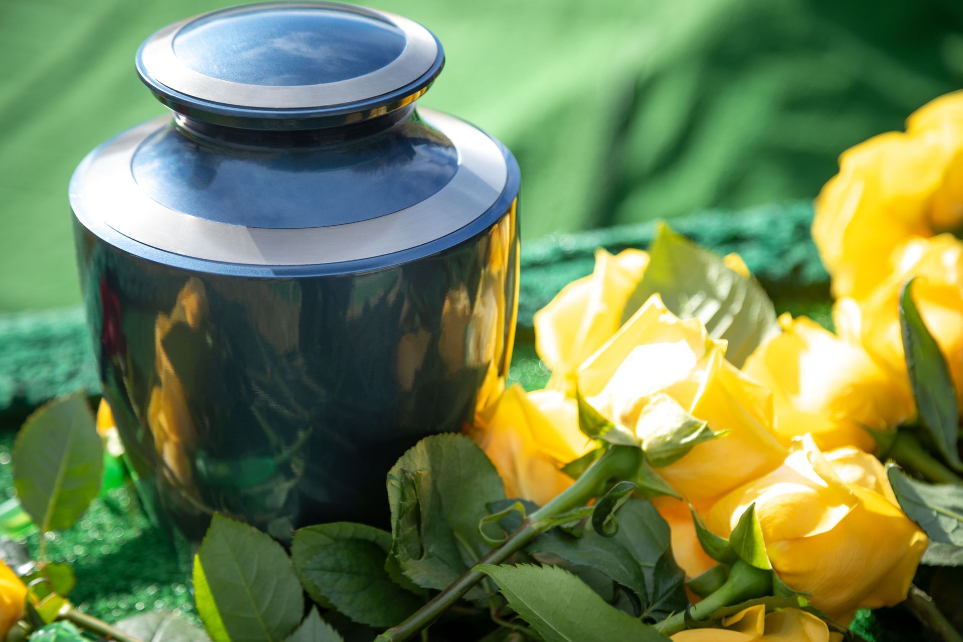 Blue urn beside yellow roses and green leaves on a green cloth background