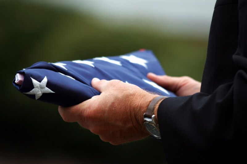Hands holding a folded American flag at a funeral-like ceremony