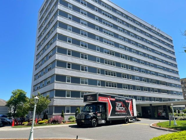 White multi-story office building with a black moving truck parked in front under a clear blue sky