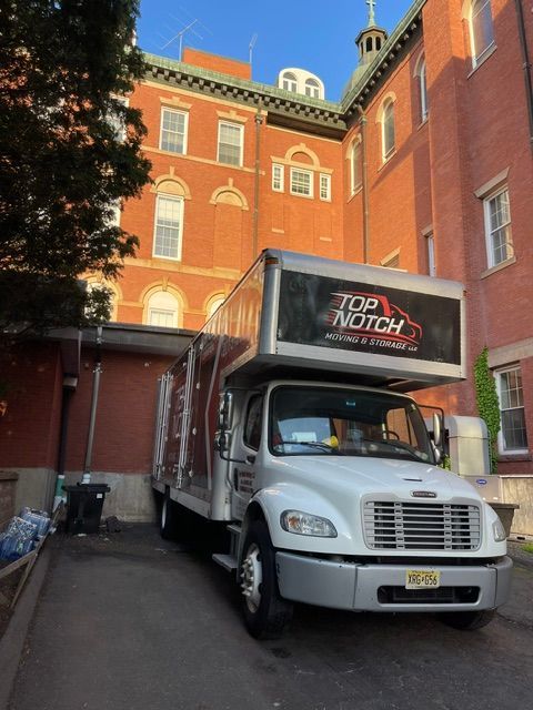 White box truck parked in a narrow alley beside a red brick building under sunny light