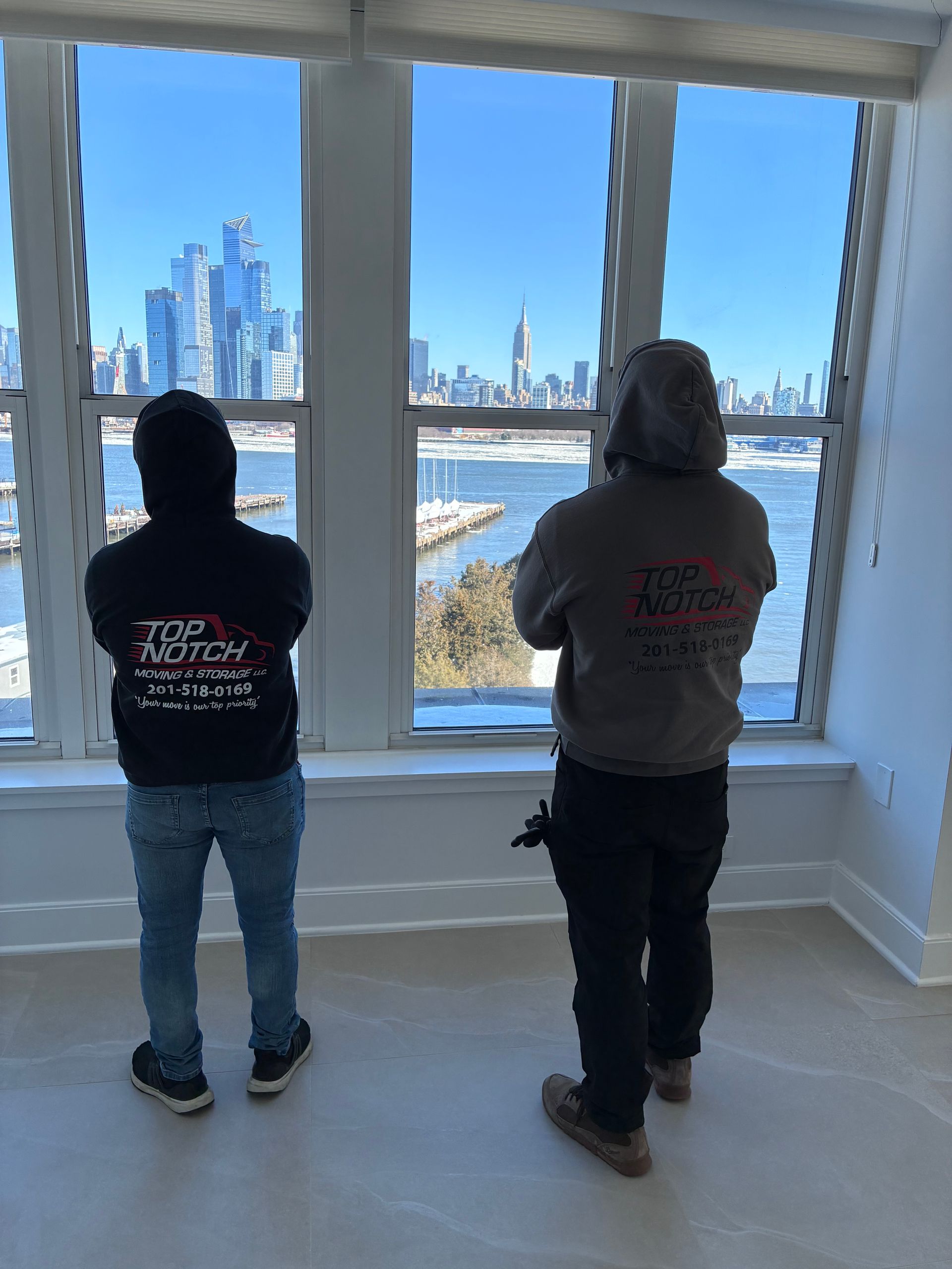 Two people in hoodies looking out a window at a city skyline over a body of water.