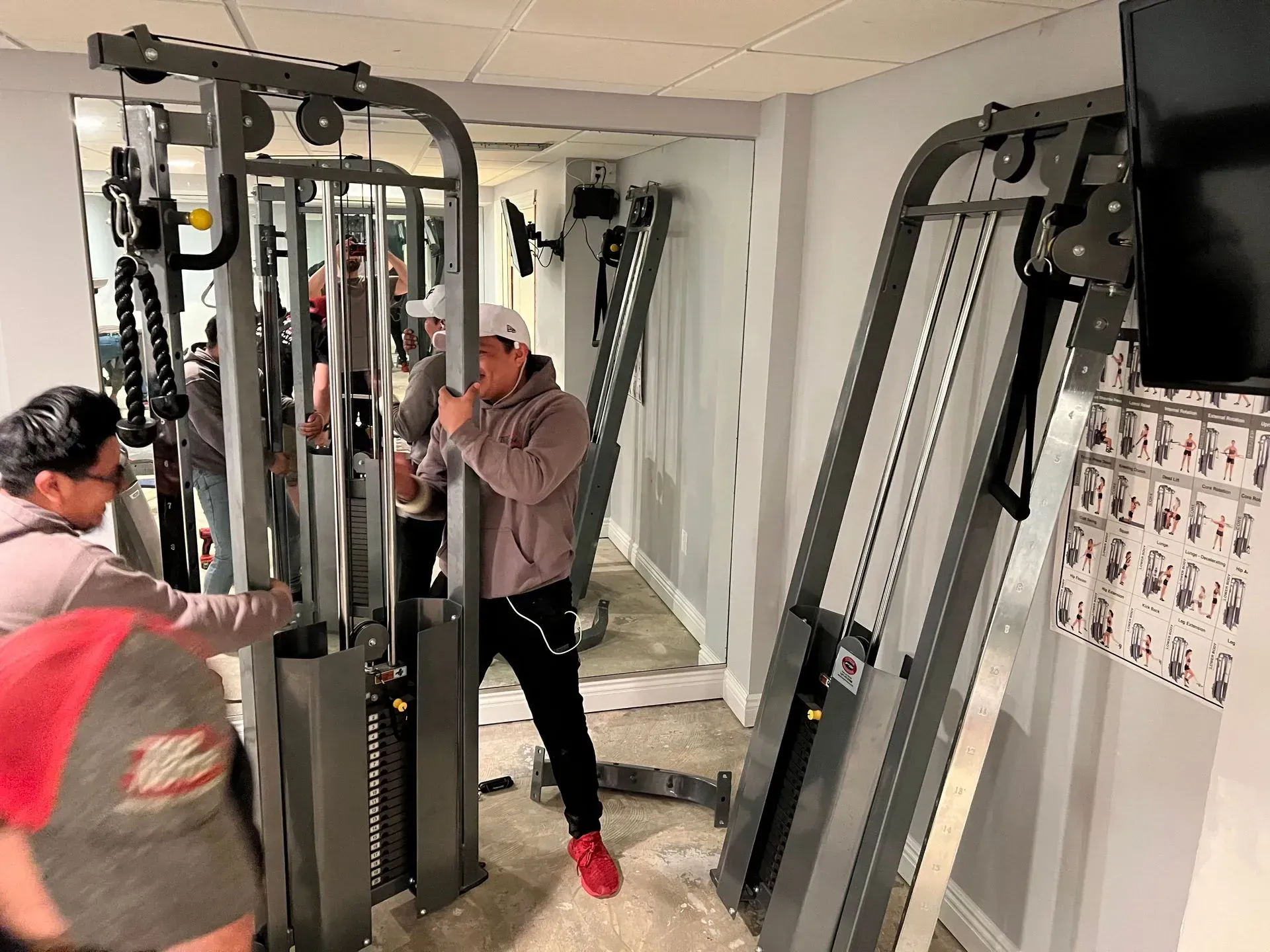 Men assemble a gym cable machine in a room with a large mirror.