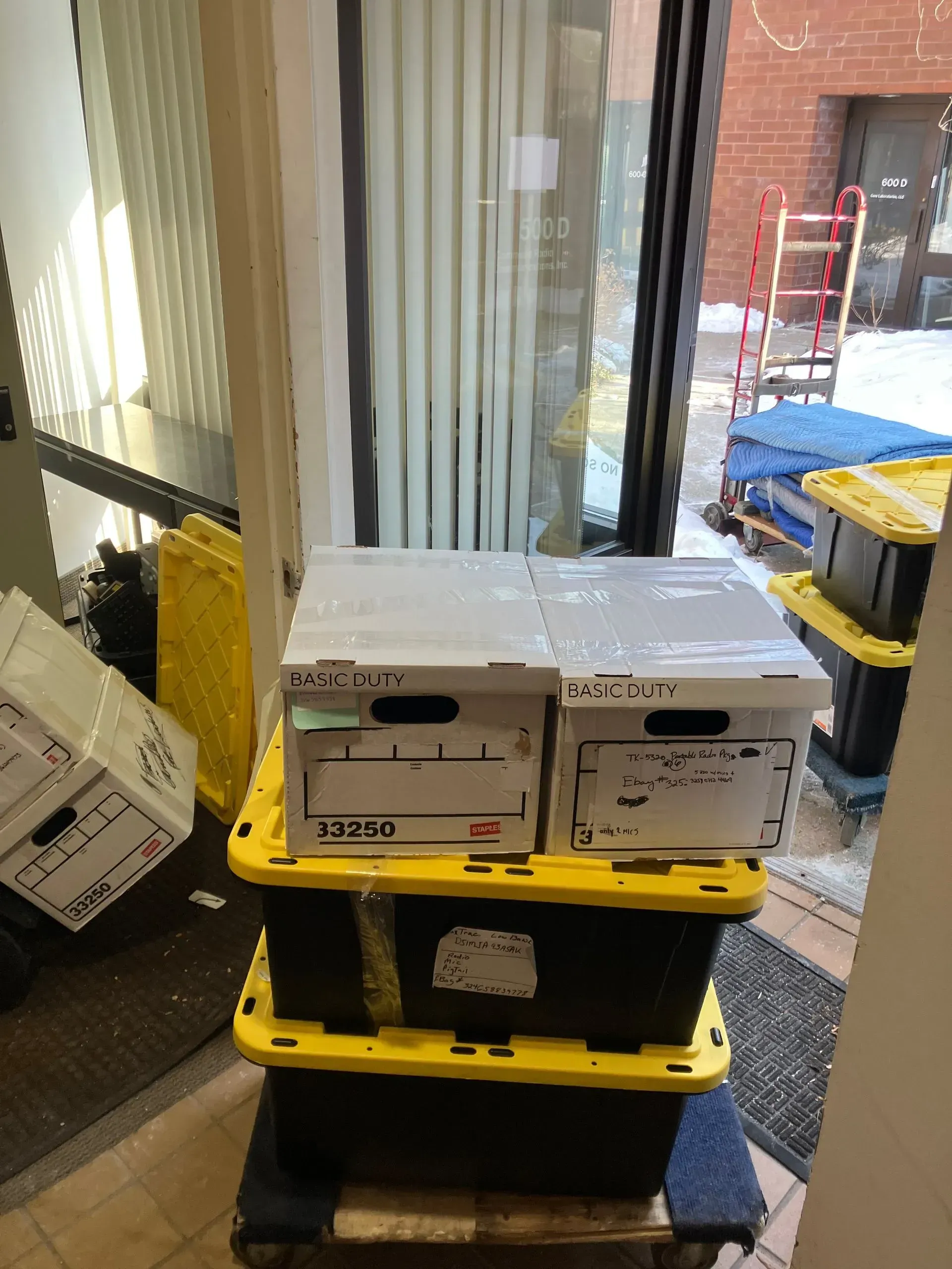 Boxes stacked on a dolly in a doorway, next to window blinds.