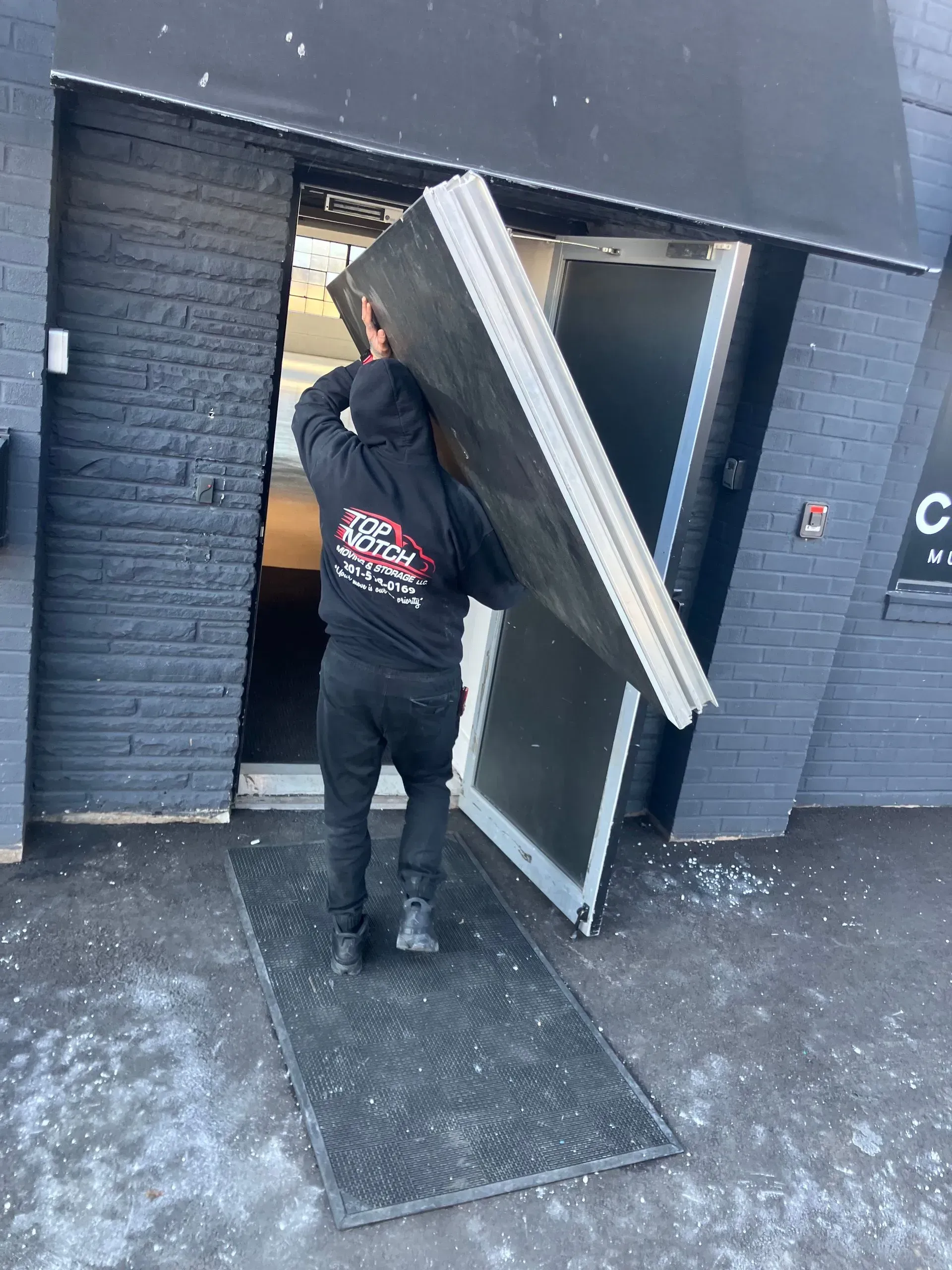 Person carrying a large door panel outside a dark building with a broken door.
