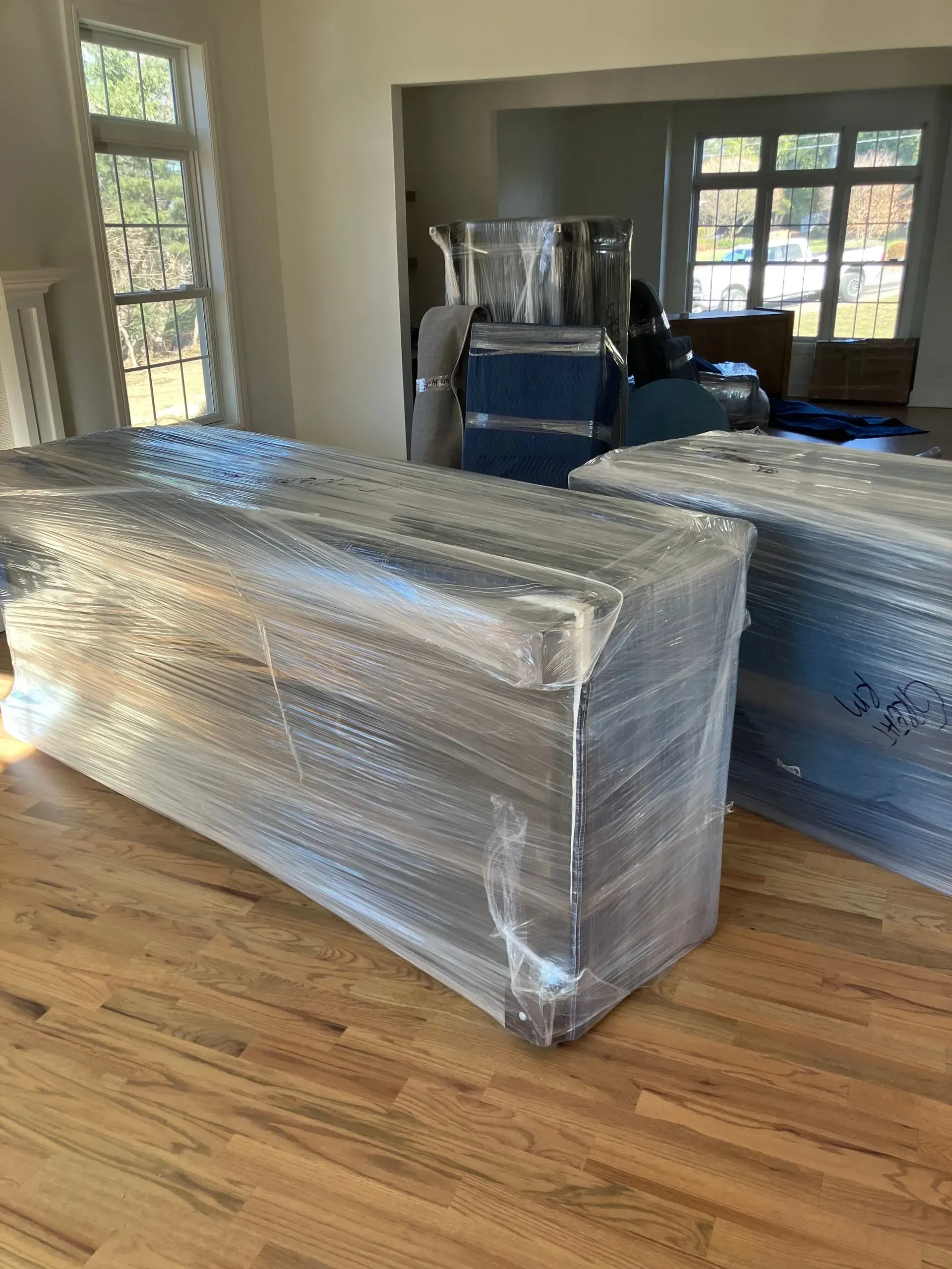 Two wrapped dressers on a wood floor, inside a room with windows.