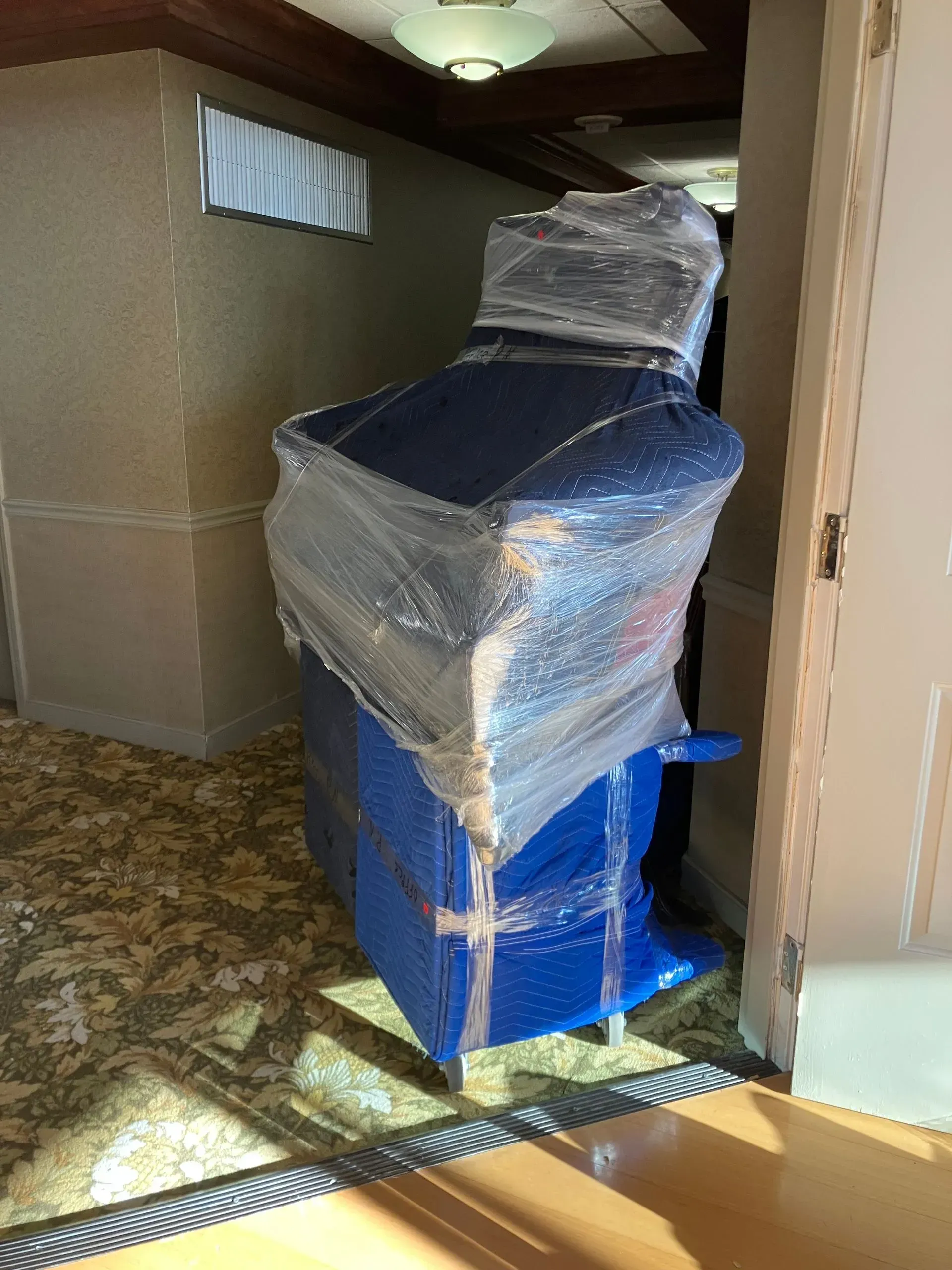Blue upholstered furniture wrapped in plastic, partially blocking a doorway in a hallway.
