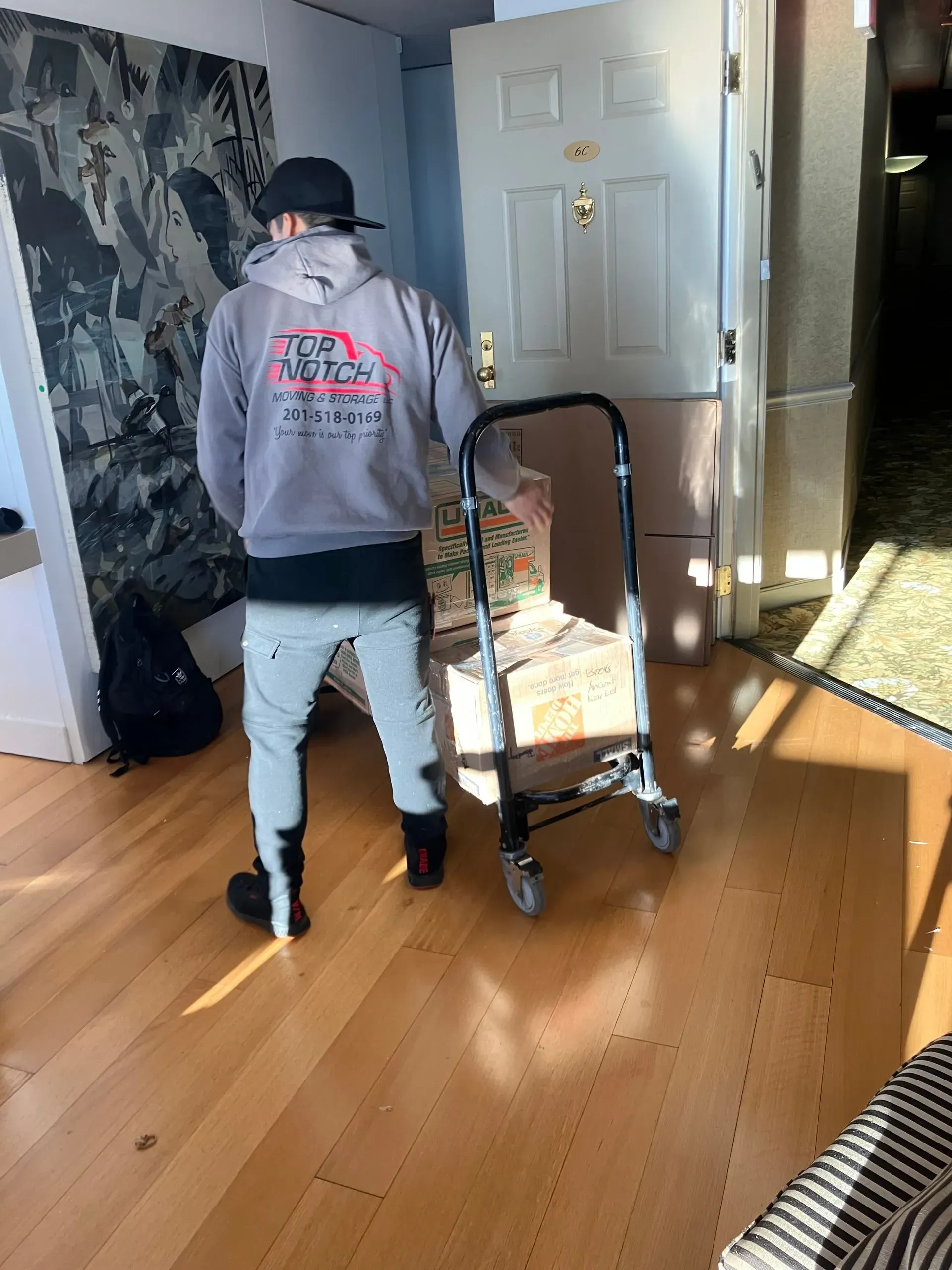 Person unloading a hand truck with boxes in a room, approaching a door.