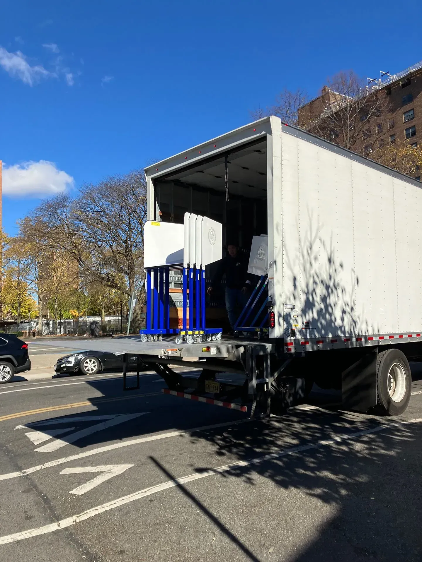 White truck with open back displaying blue shelving and boxes parked on a street.