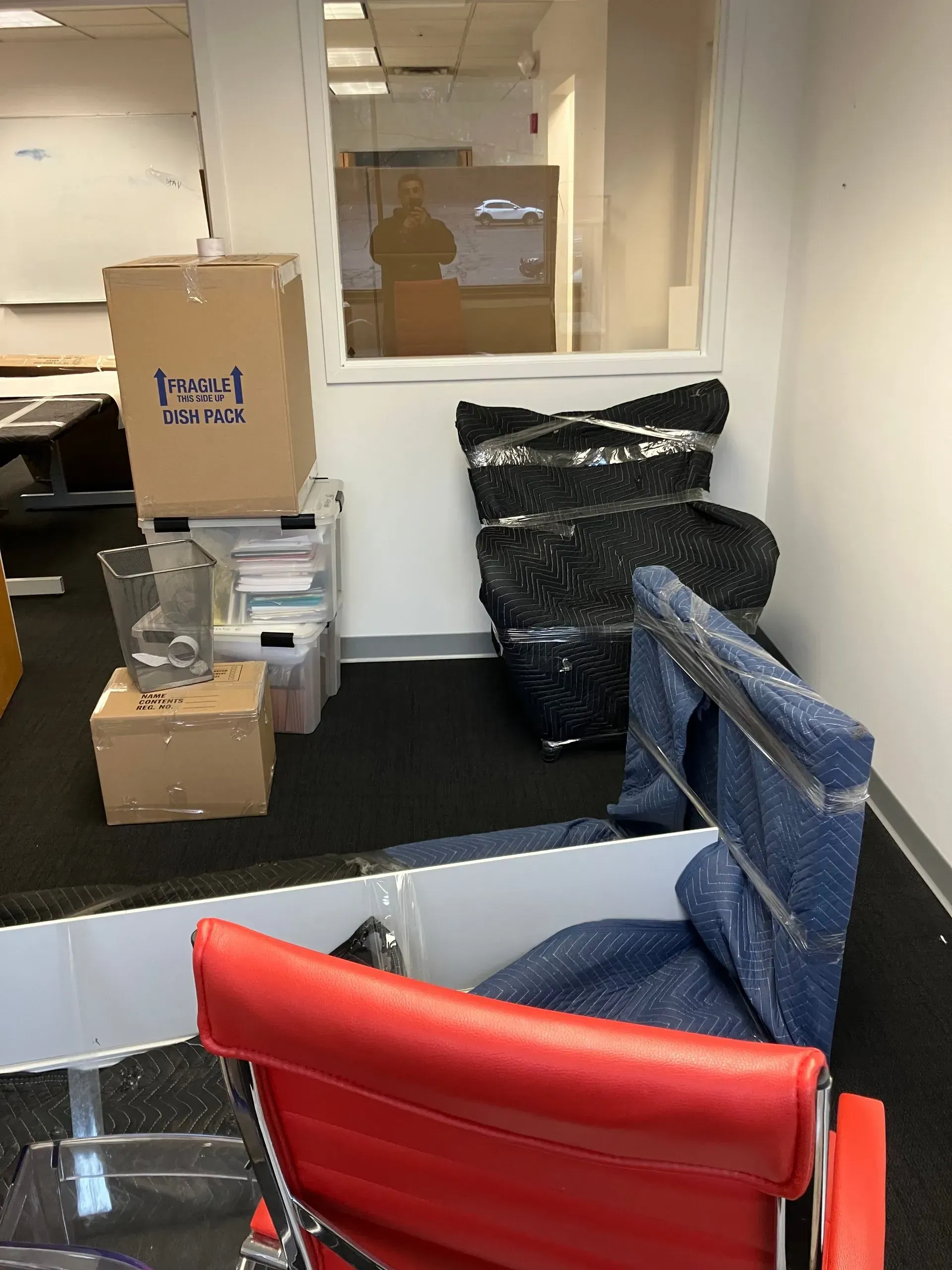 Office scene with boxes, a wrapped item, and a red chair.