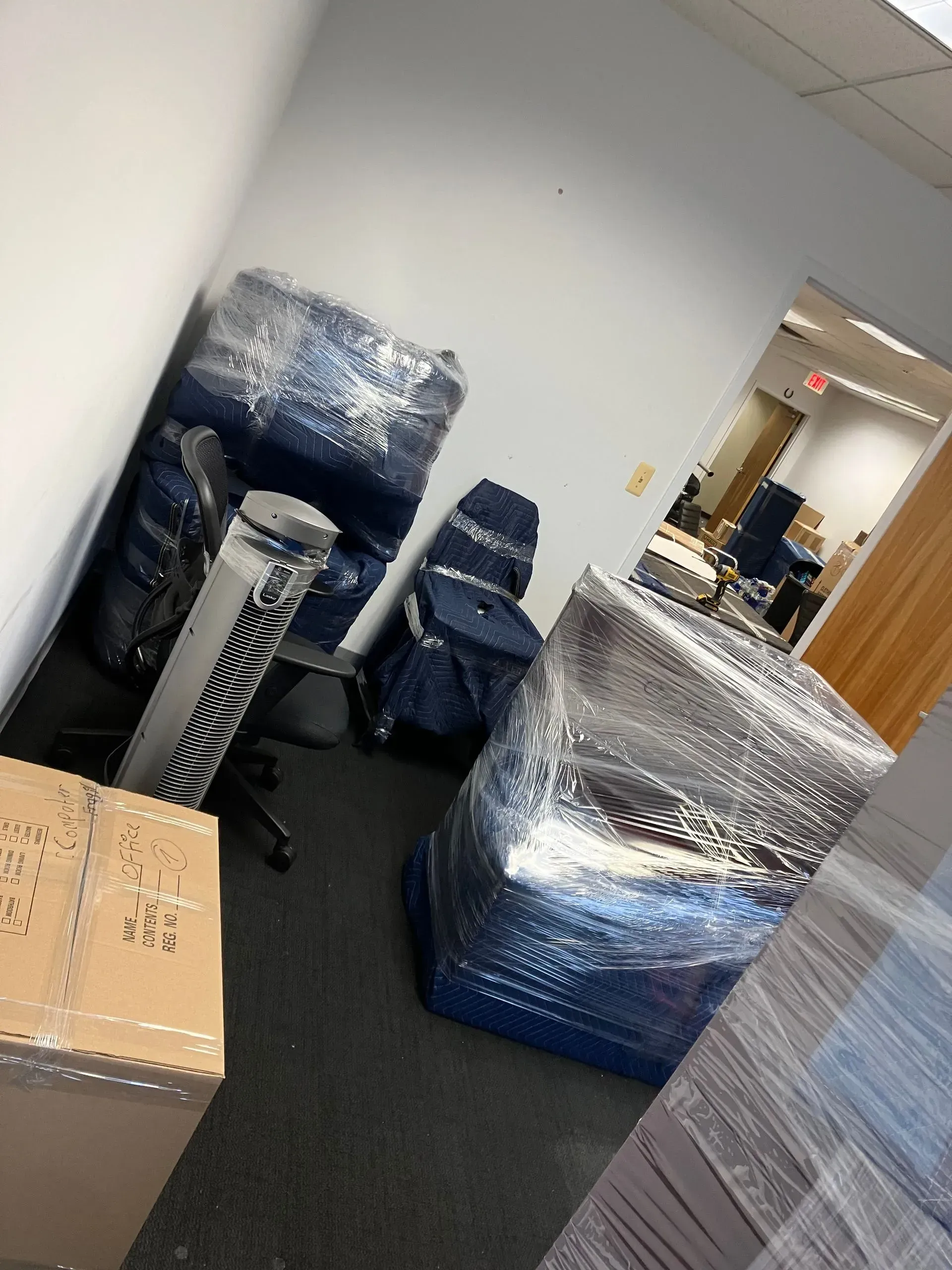 Office furniture wrapped in plastic, ready for moving; boxes in foreground.