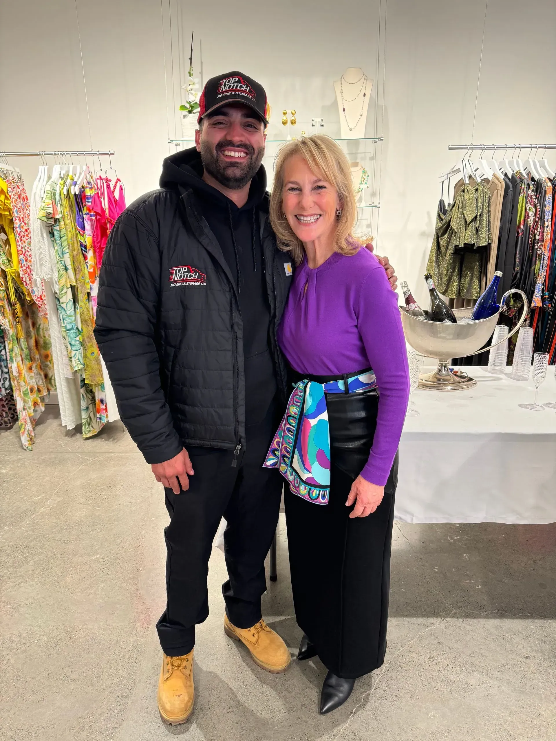 Man in black jacket and woman in purple top pose in clothing store.