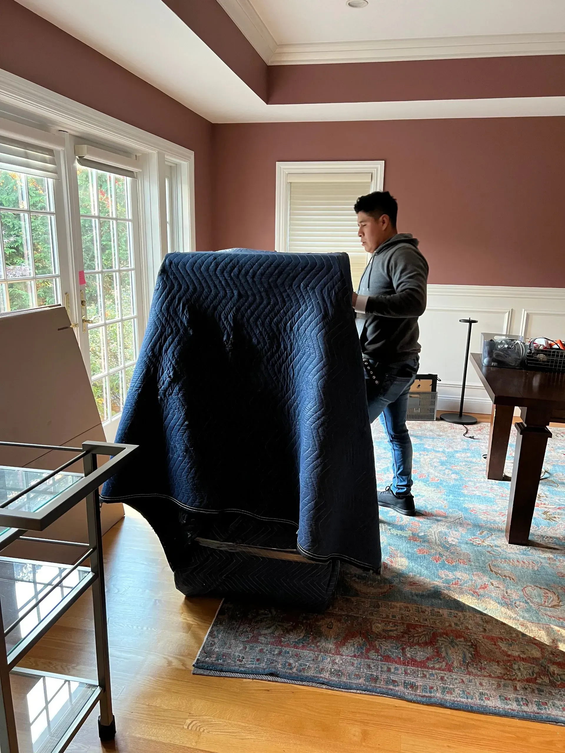 Person moving a large, covered object in a room with hardwood floors and a rug.