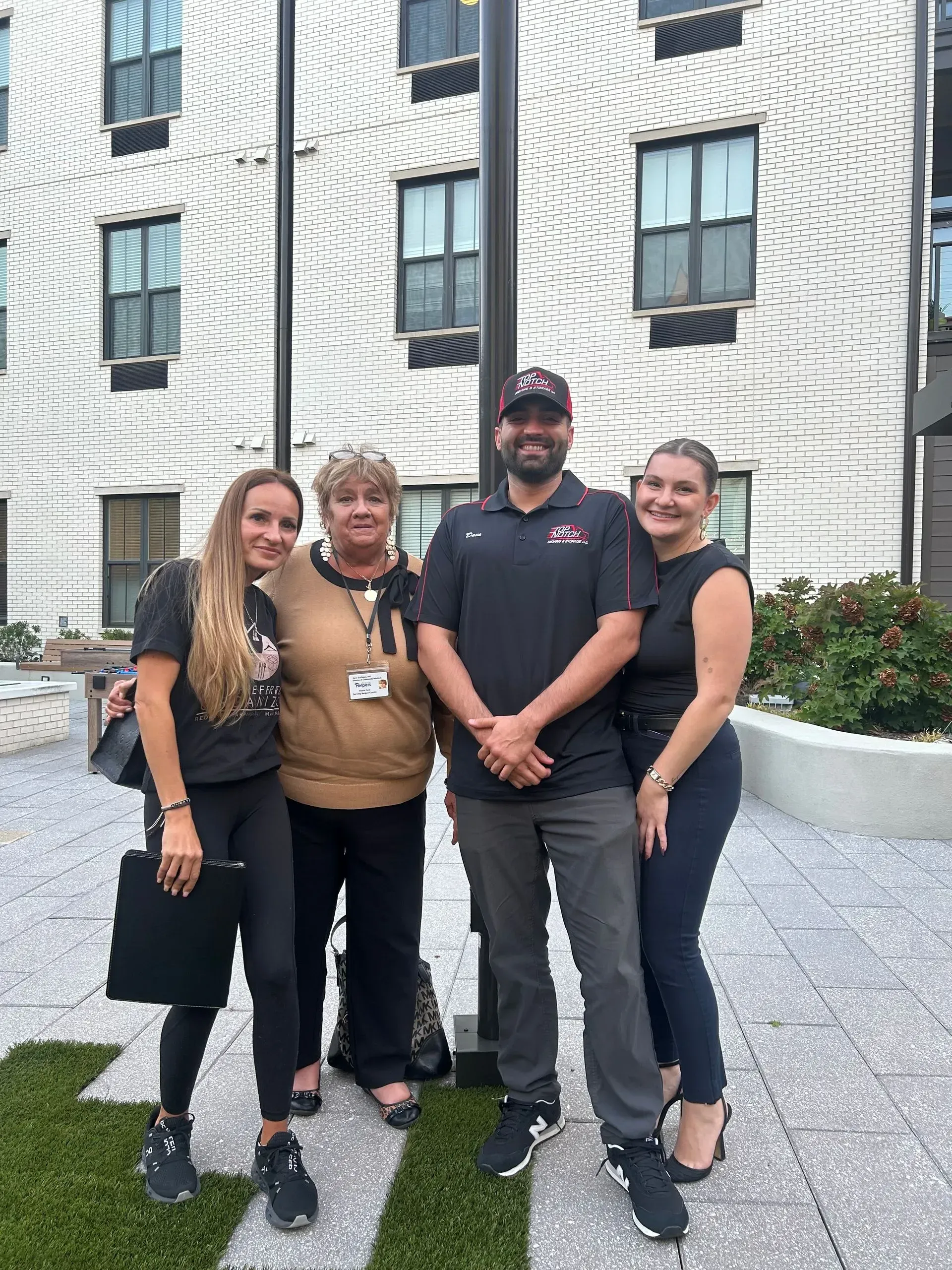 Four people standing outdoors near a building; two women and two men.