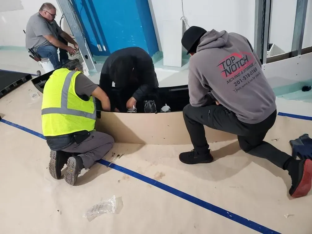 Four people installing a structure in a room with blue accents. One wears a reflective vest.