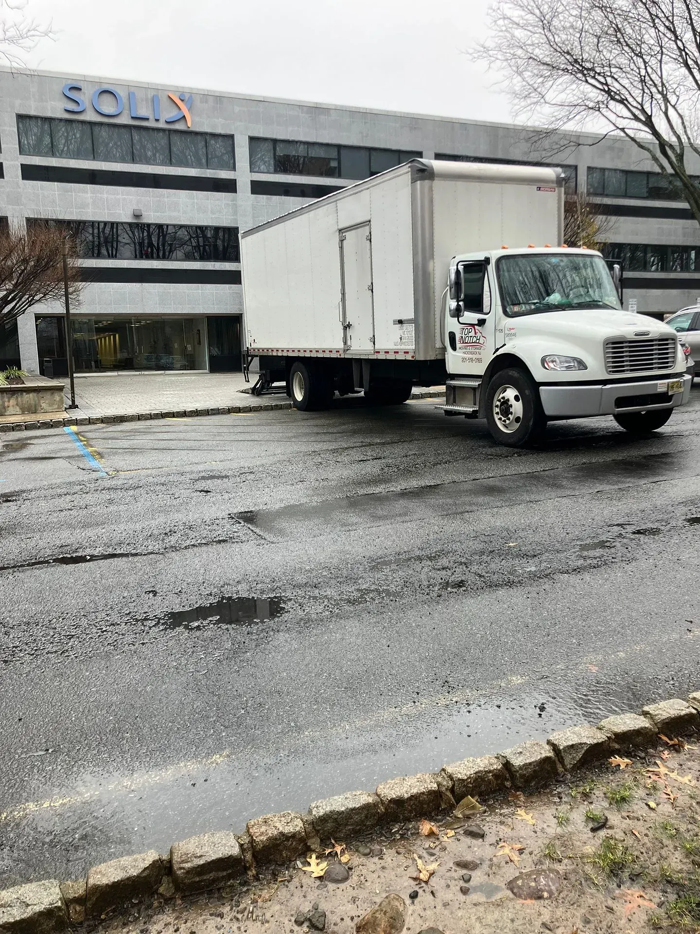 White box truck parked in front of a building with SOLIS signage on a wet, paved surface.
