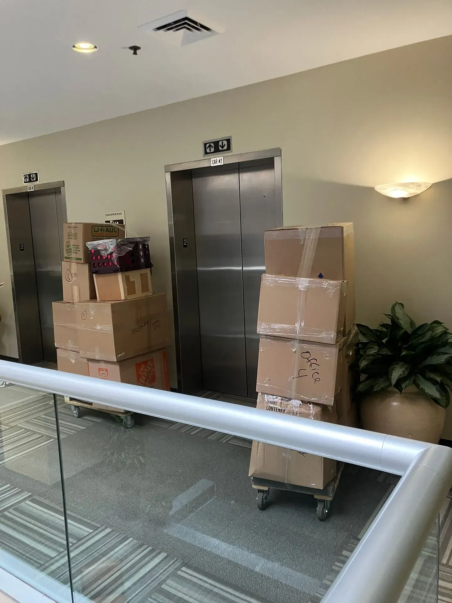 Two elevators in a hallway, with boxes stacked on rolling carts in front of them.