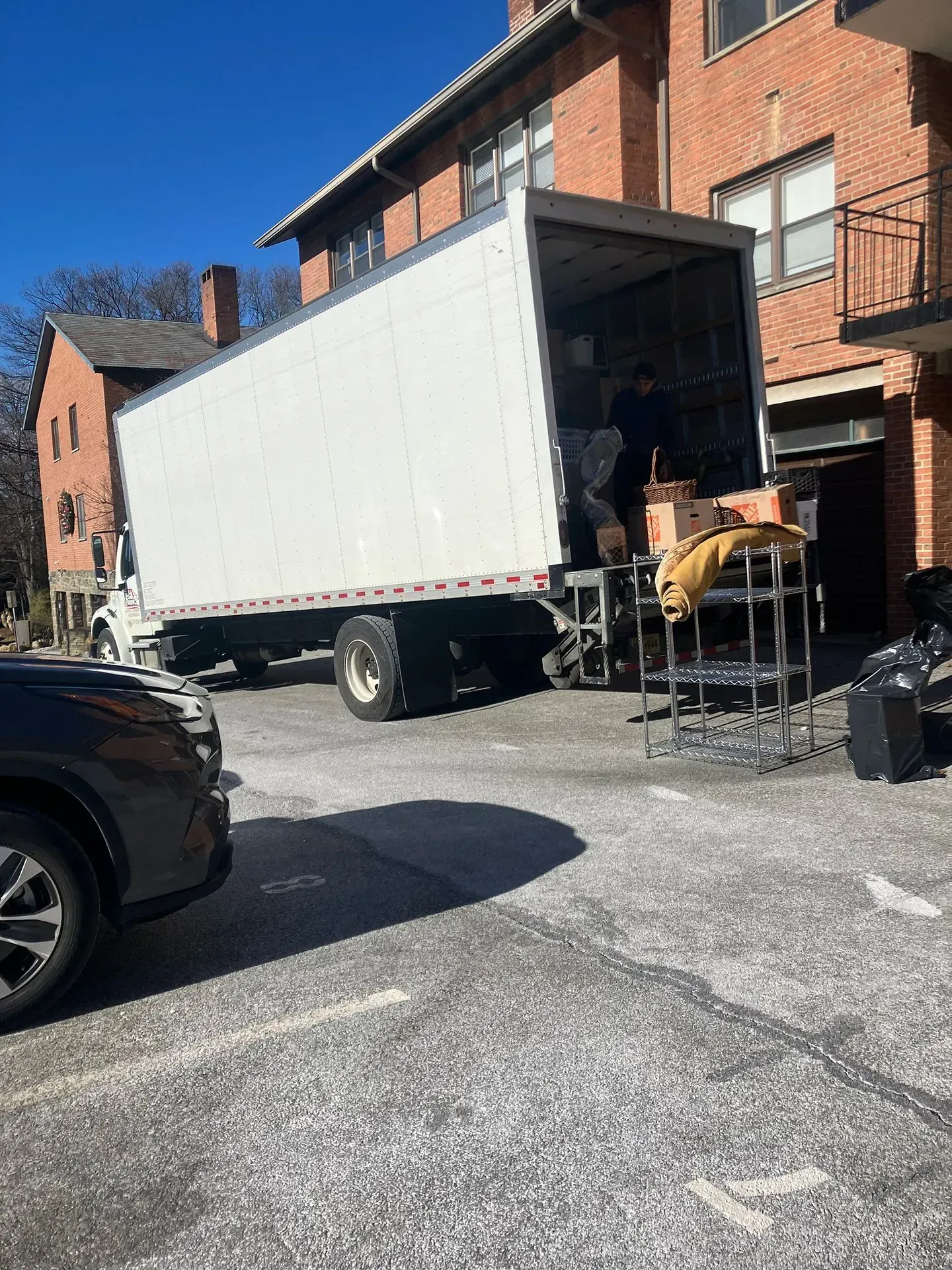 Moving truck parked near a brick building; worker loading furniture into the truck.