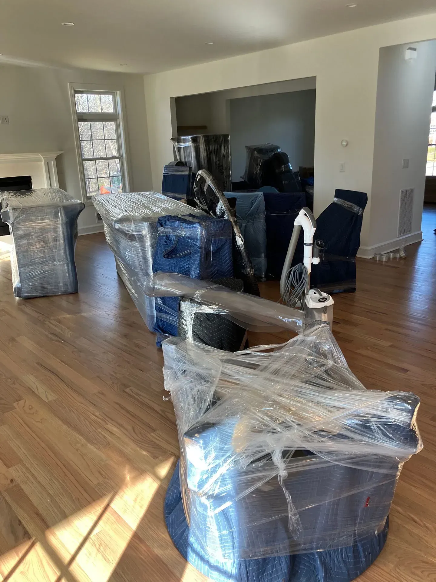 Furniture wrapped in blue padding and plastic, in a room with hardwood floors, ready for transport.