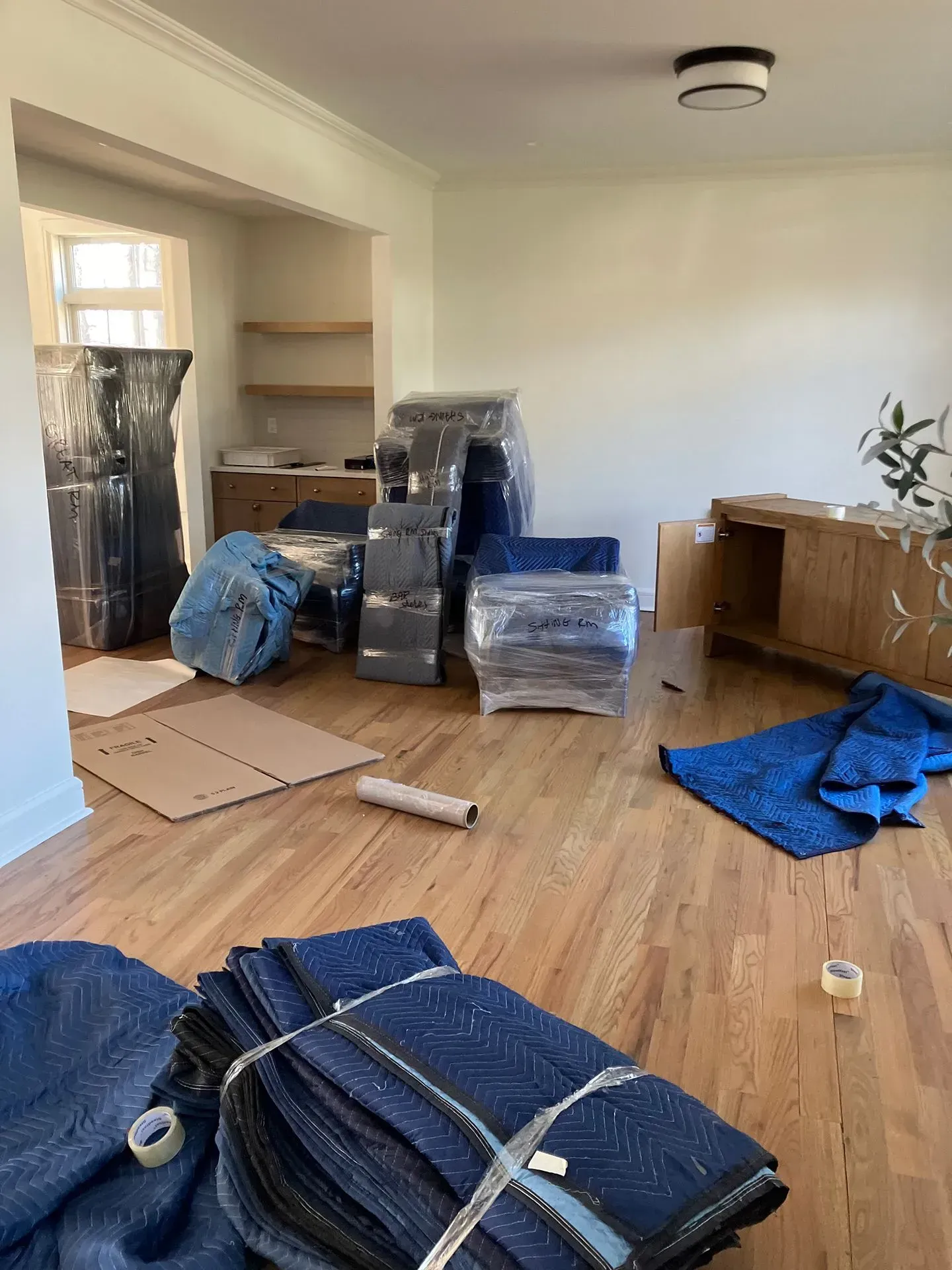 Room with furniture wrapped in plastic and moving blankets, ready for transport.