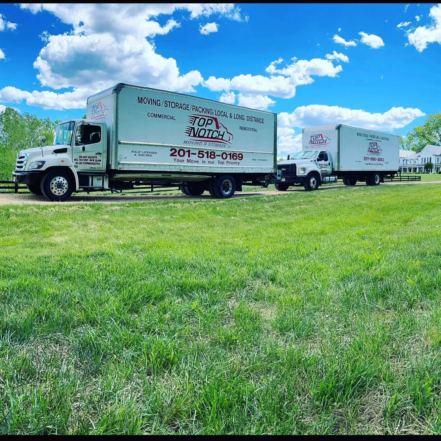 White moving trucks on a grassy field under a blue sky with clouds. 201-515-5169 is on the truck.