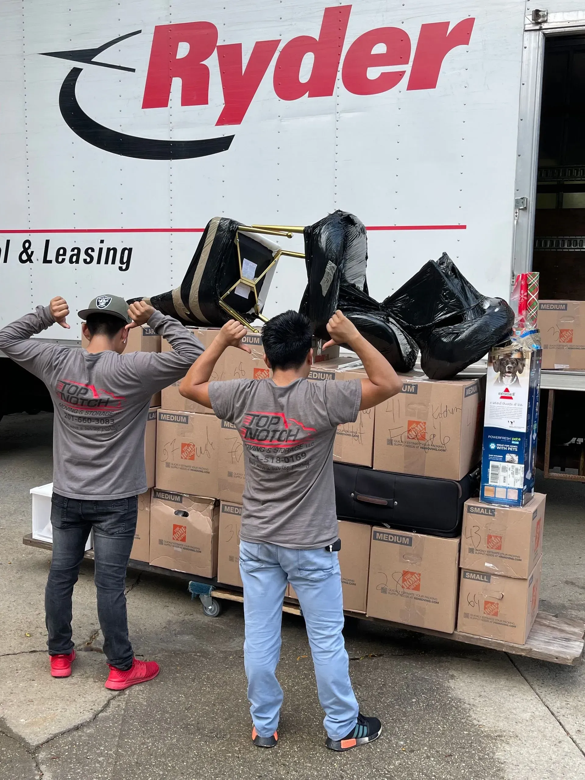 Two men flexing near a Ryder truck filled with boxes.