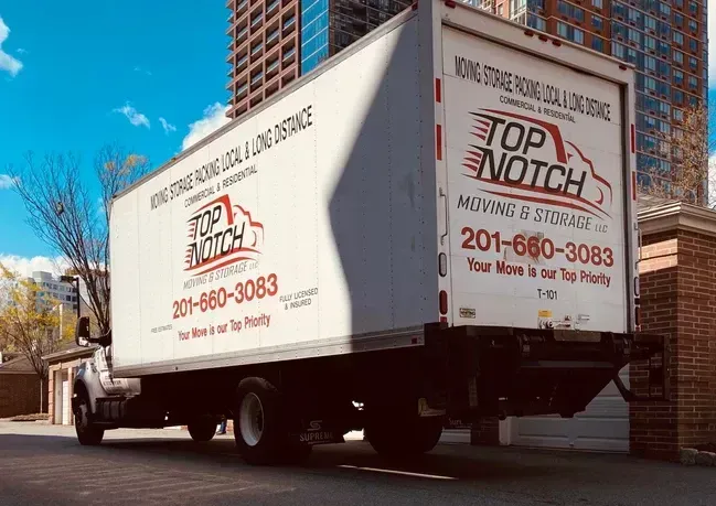 White Top Notch Moving & Storage truck parked on a street with high-rise buildings in the background. The phone number 201-660-3083 is displayed.