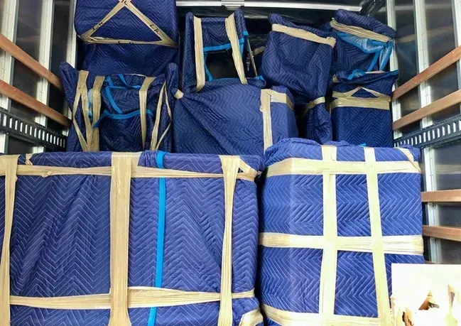 Moving truck interior packed with furniture wrapped in blue pads, secured with tape.
