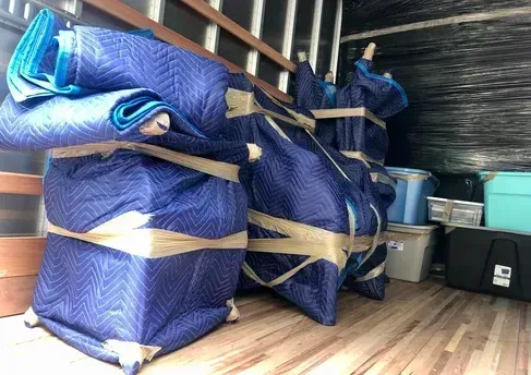 Blue padded furniture wrapped and secured with tape inside a moving truck.
