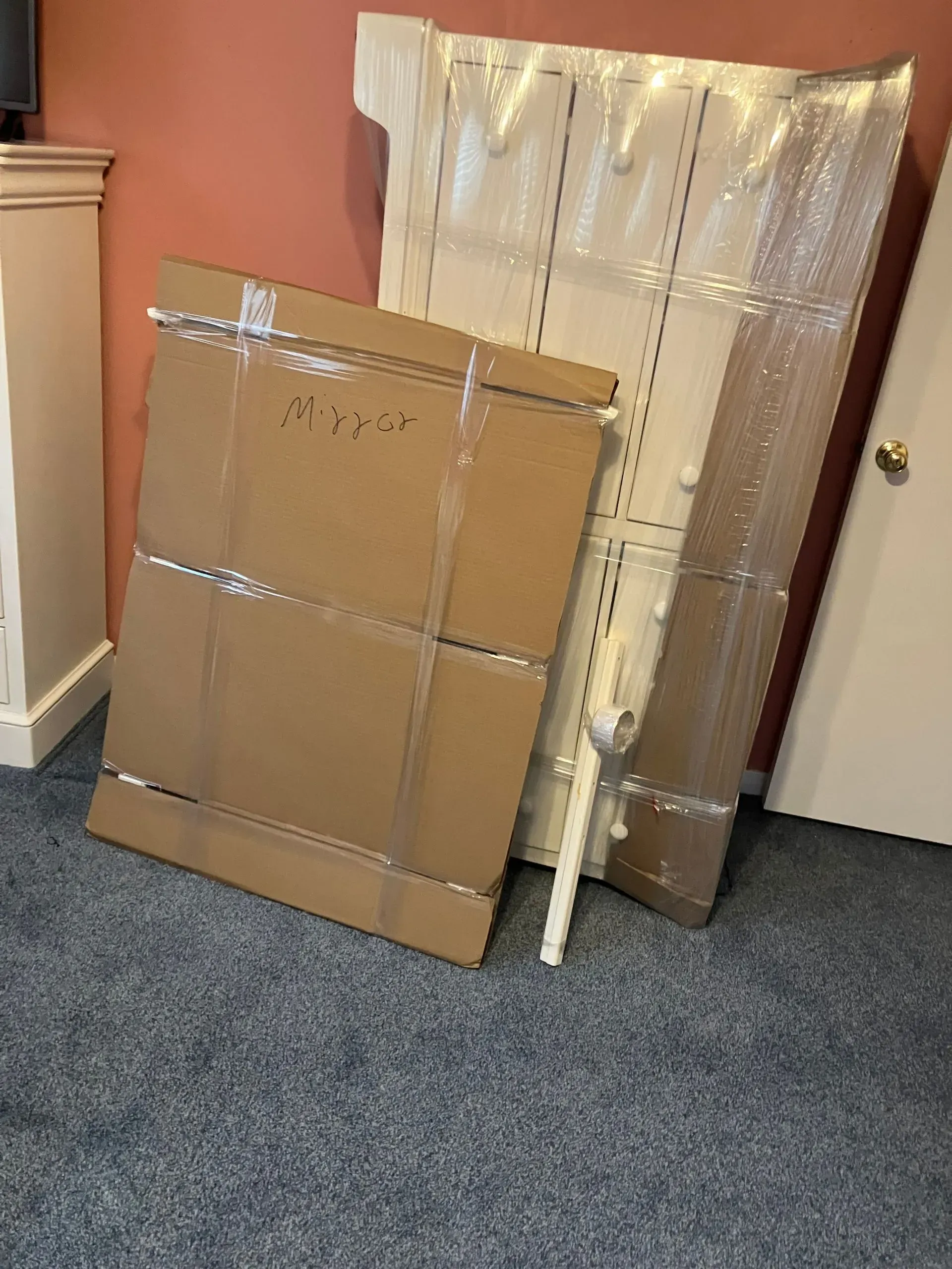 Cardboard boxes and wrapped furniture leaning on a wall in a room with blue carpet.