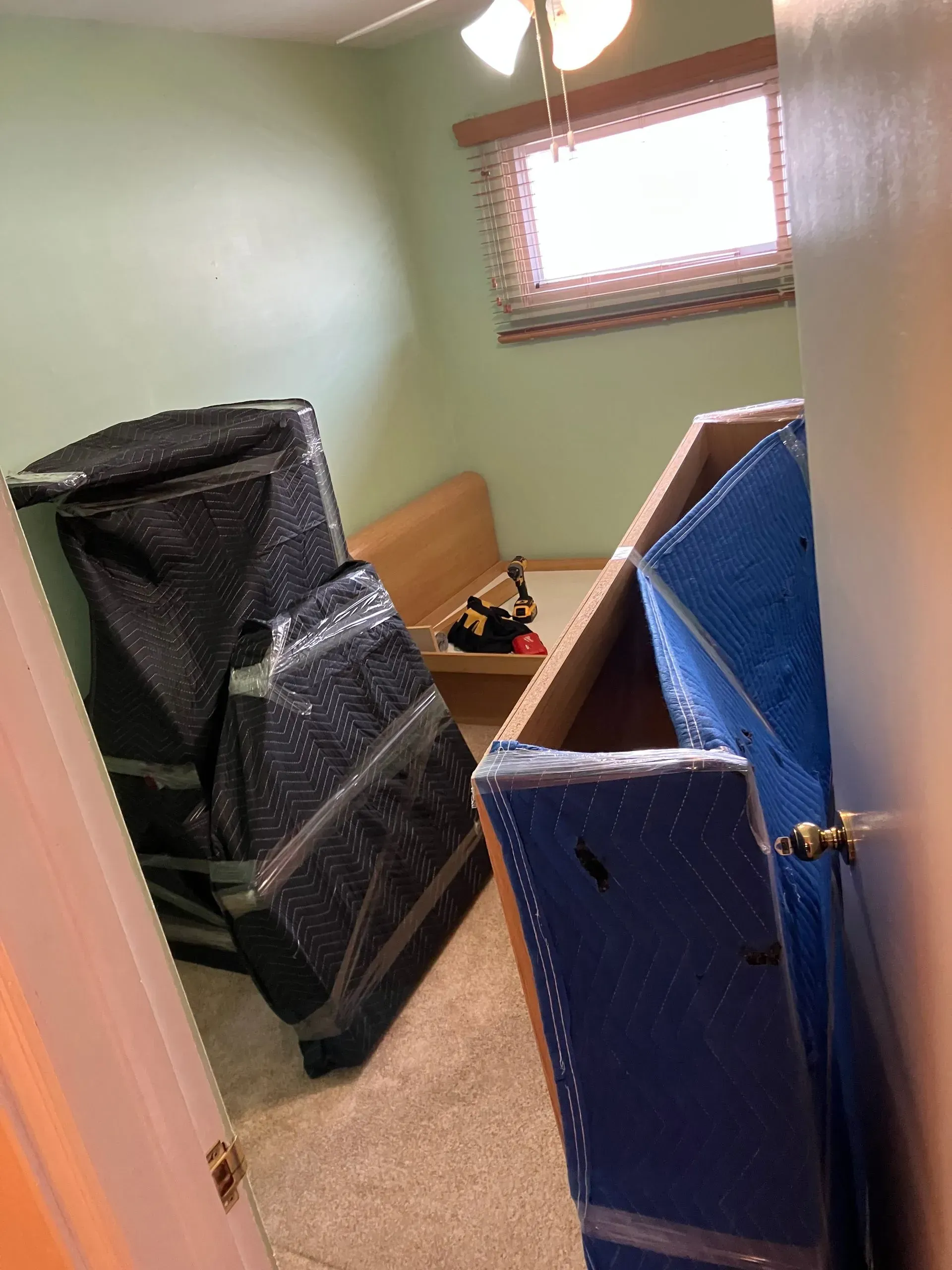 Boxes and wrapped furniture in a room with a bed, ready for a move.