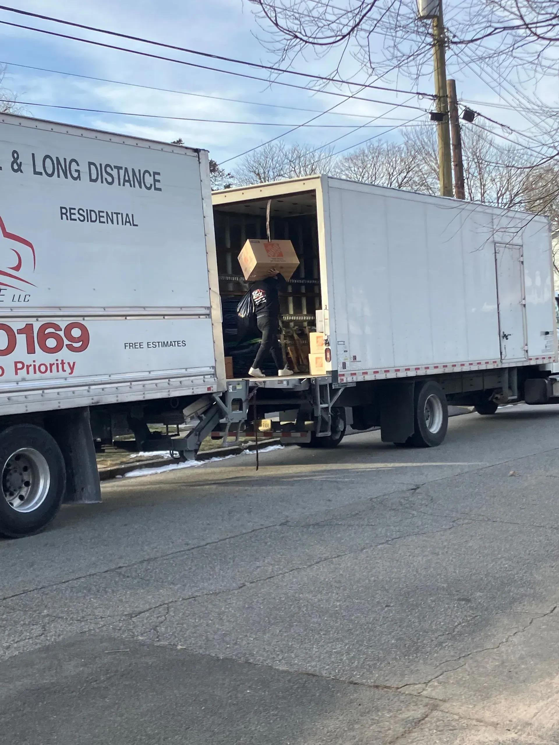 Moving truck with open cargo area. A cardboard box is being lifted inside. Outdoor setting, overcast sky.