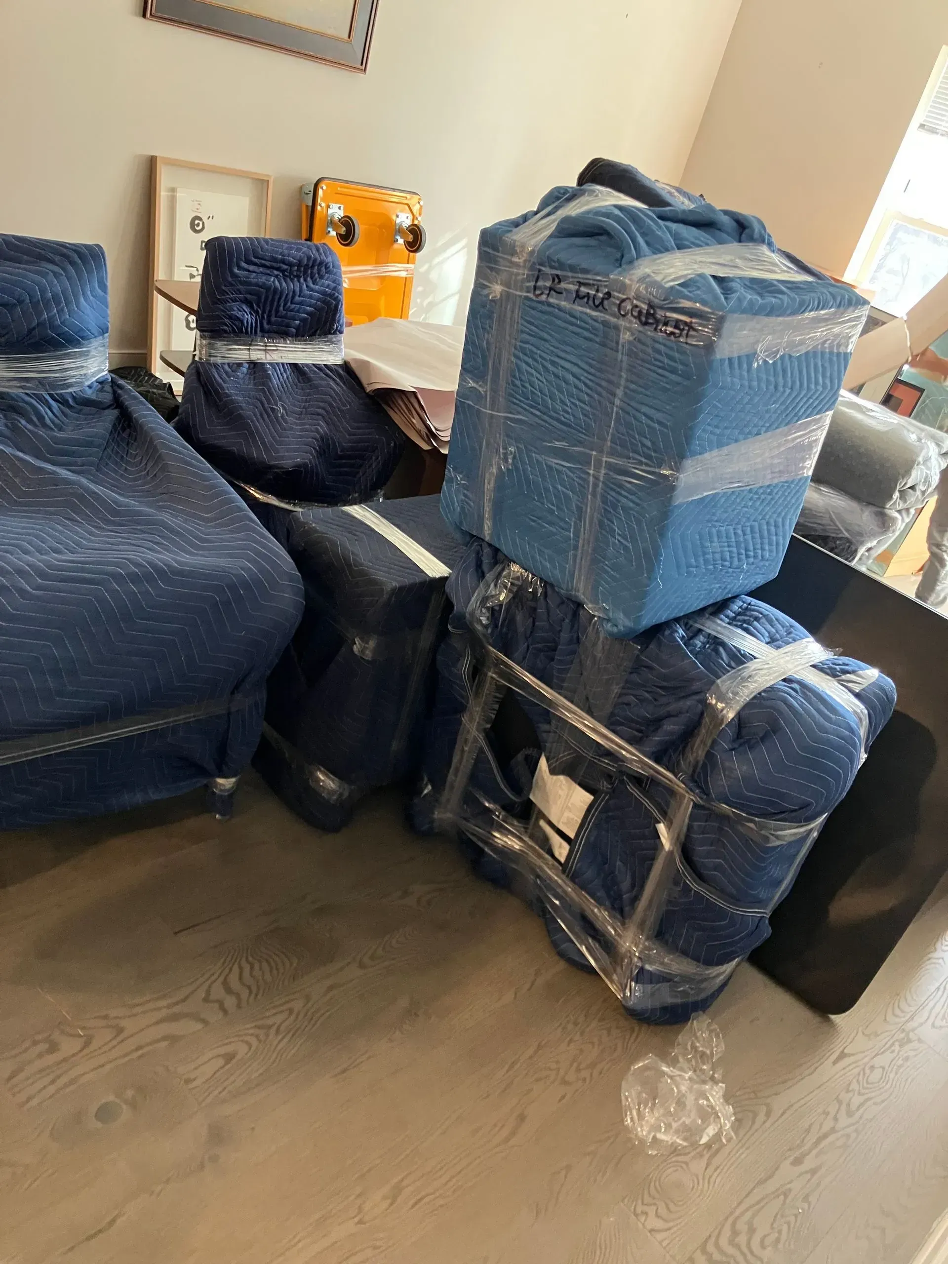 Boxes and furniture wrapped in blue packing material, secured with tape, ready for transport.