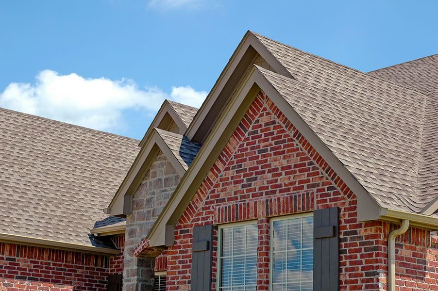 a brick house with a brown roof and shutters on the windows .