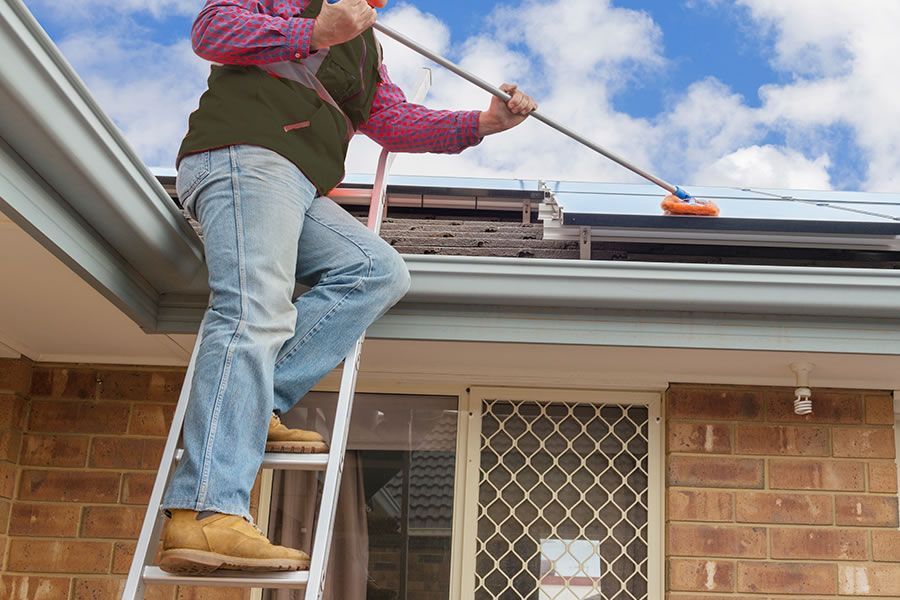 a man is standing on a ladder cleaning the gutters of a house .