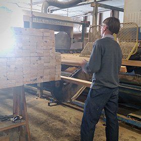Person in a factory setting, operating machinery with a large wooden block.