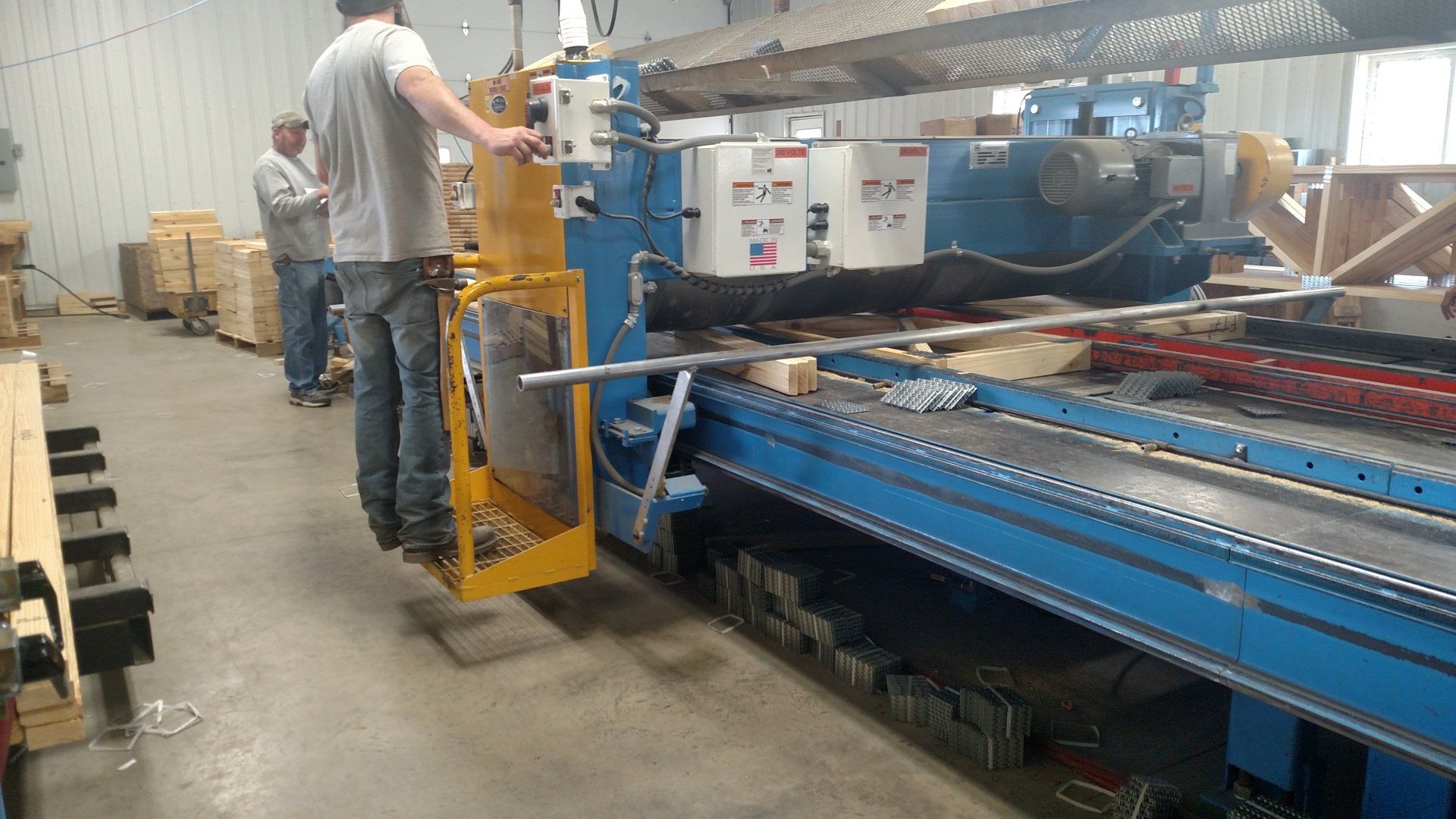 Man operating industrial machine in a warehouse, another man watches.