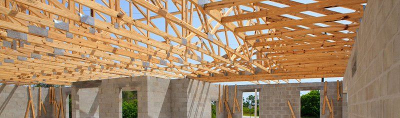Construction site of a building's interior. Wooden roof beams and concrete block walls are visible. The sky is seen through openings.