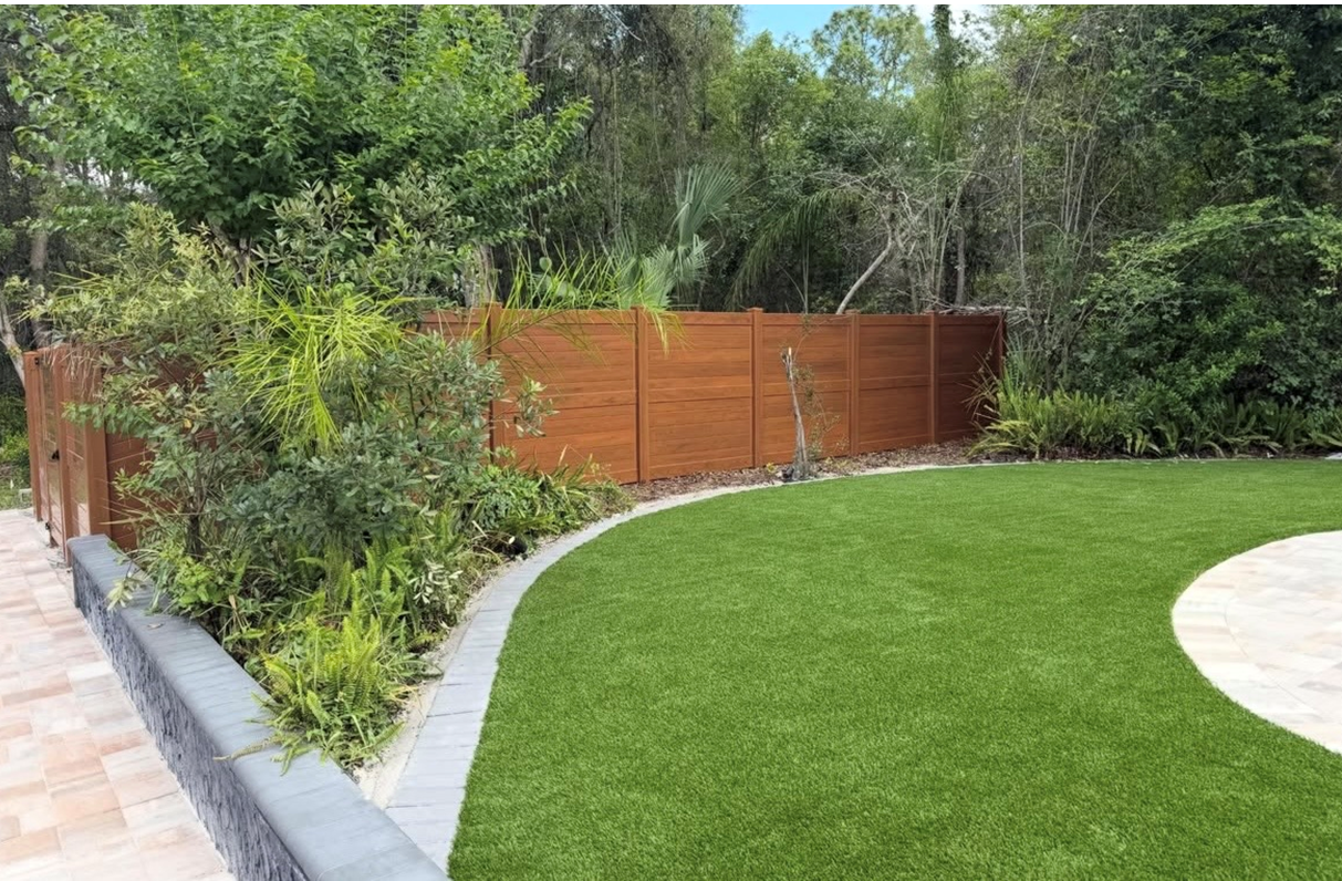 Curved green lawn beside a wooden fence and garden path with trees in the background