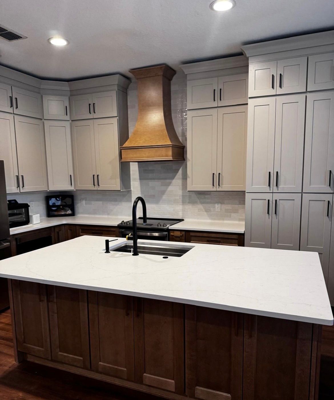 Modern kitchen with white cabinets, wood island, stainless hood, and white countertop with black sink fixture
