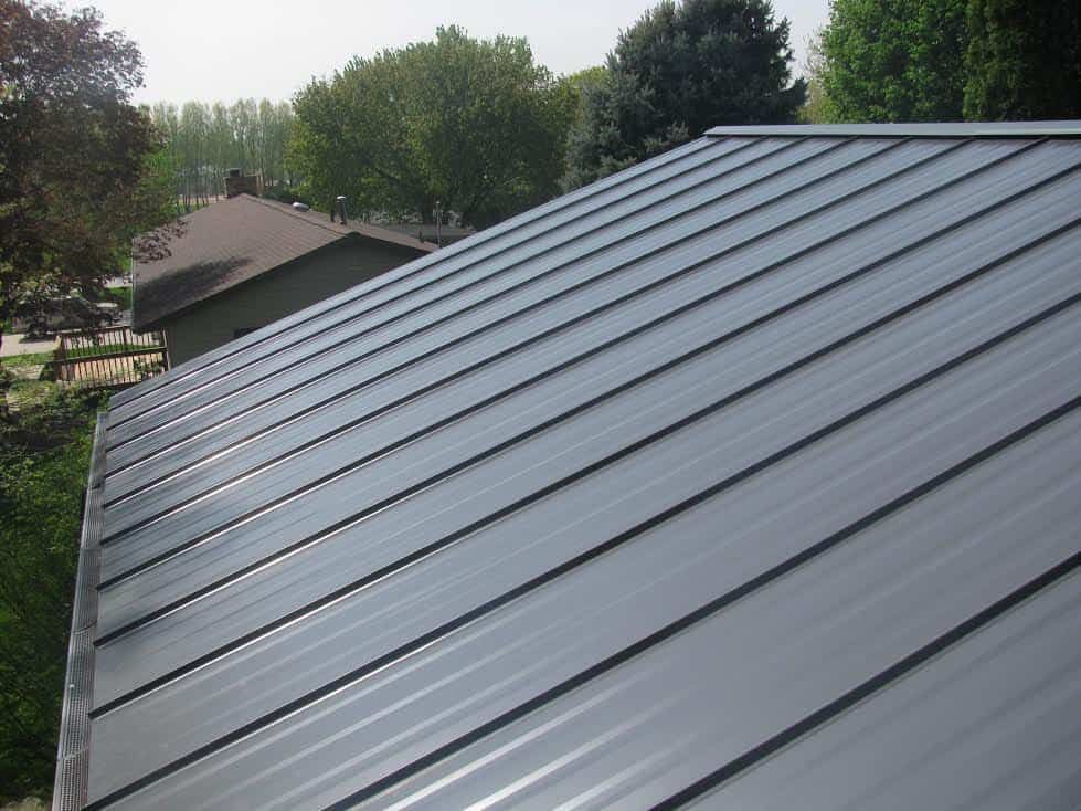 A close up of a gray metal roof with trees in the background.