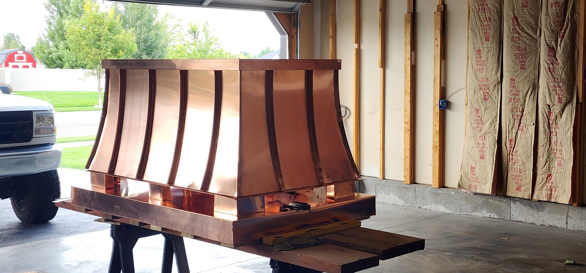 A copper chimney hood is sitting on a wooden table in a garage.