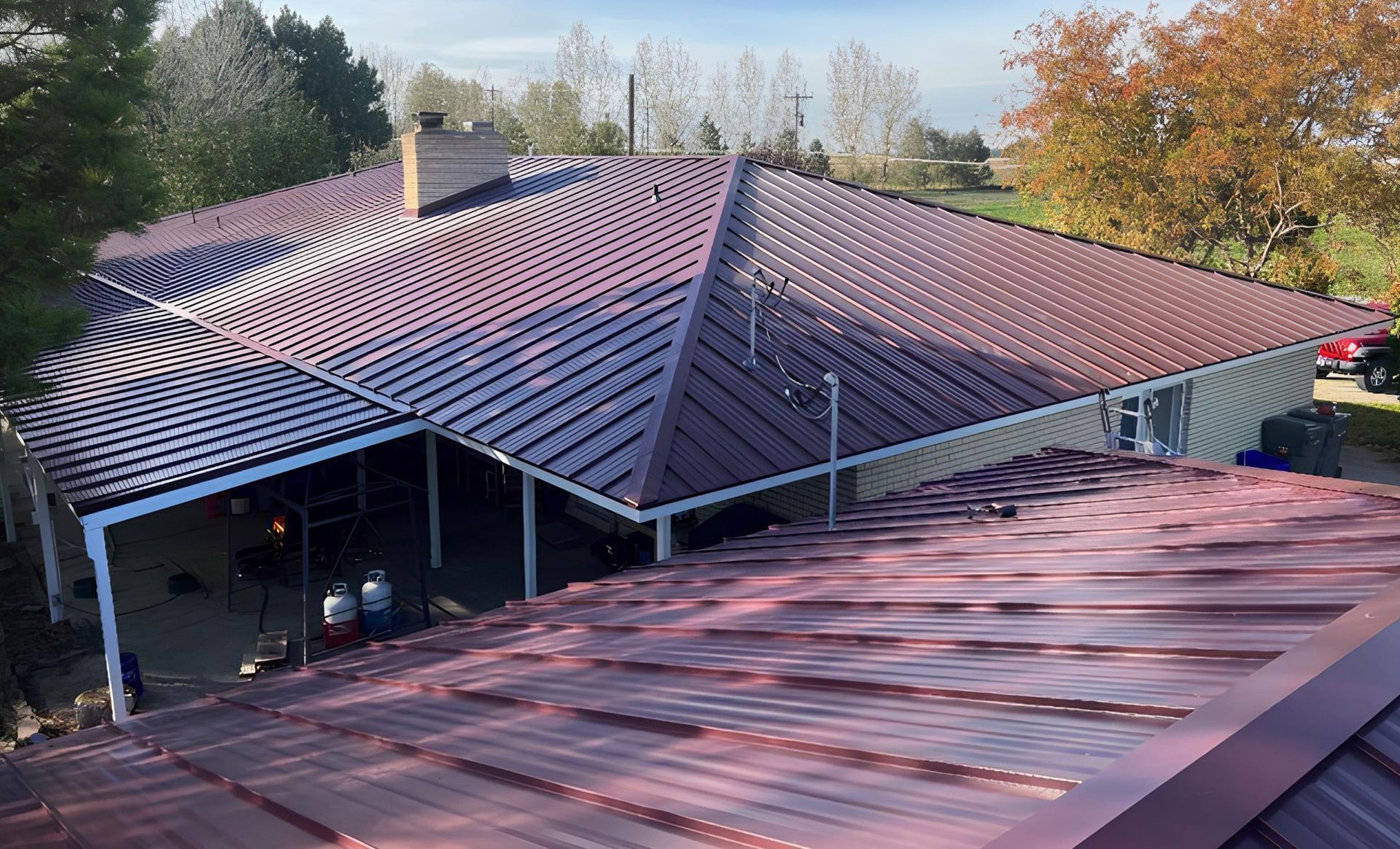 Red metal roof with curved design on a house, sunny day.