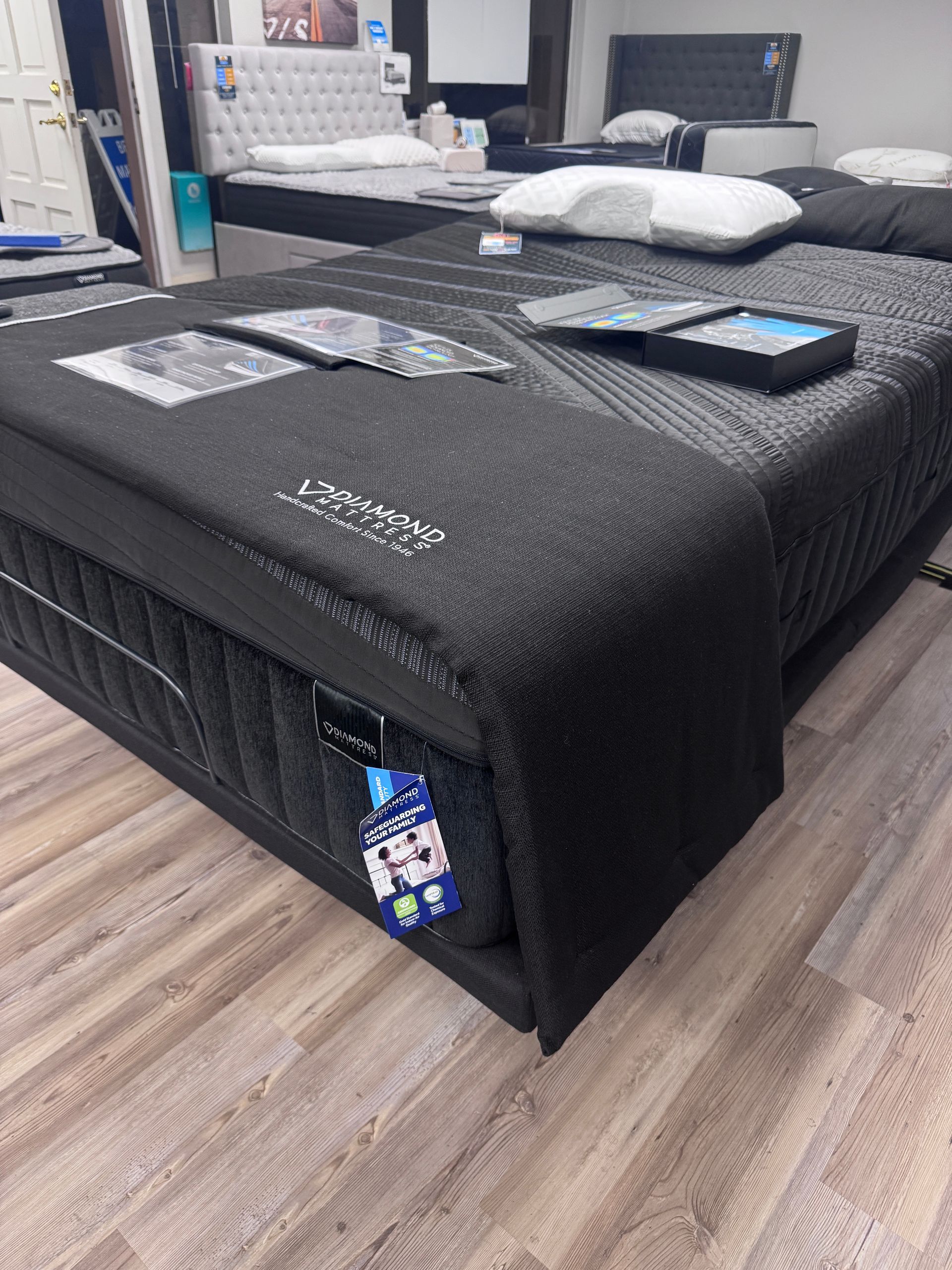 Black mattress in a showroom. Two other beds are in the background, light-colored flooring.
