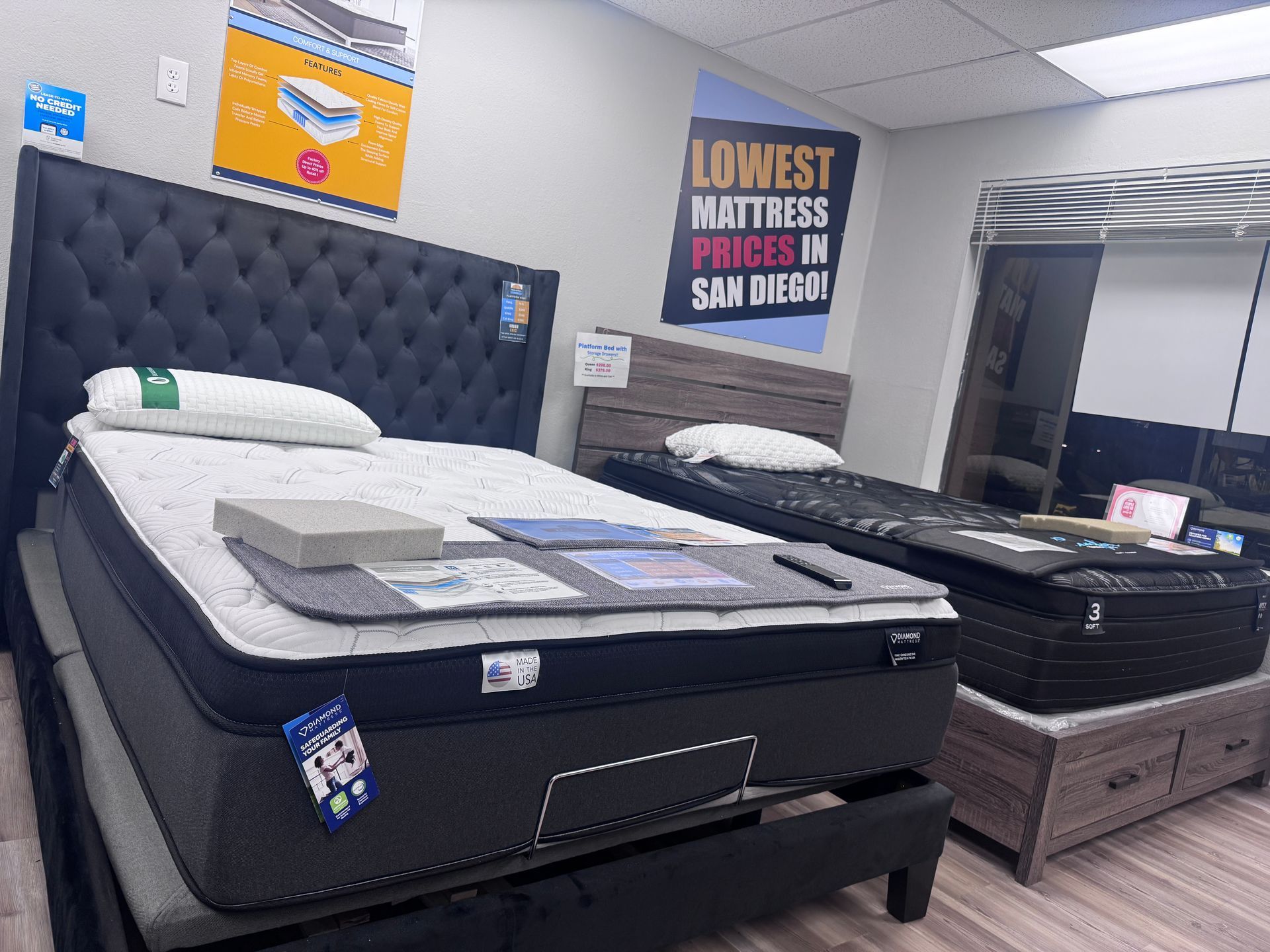 Mattress store interior with two beds. One has a tall, tufted headboard. Sign reads 