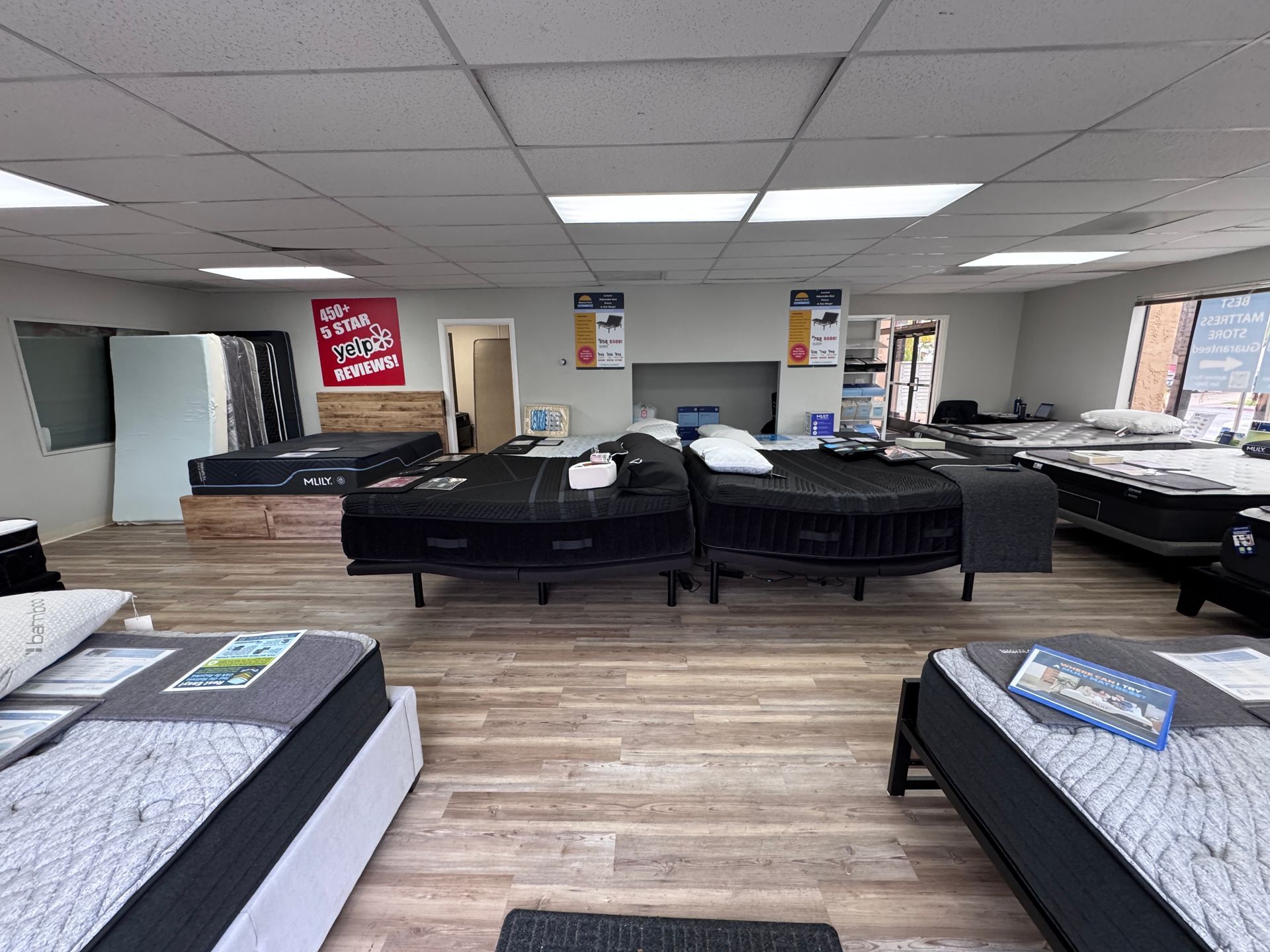 Mattress store interior with multiple beds on display; overhead lighting, wood flooring.